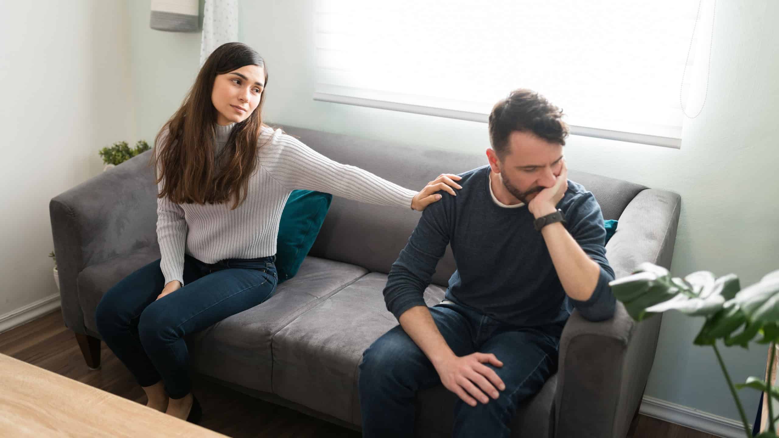 Beautiful young woman touching the shoulder of her angry handsome boyfriend while asking for forgiveness and saying sorry after having an ugly fight at home