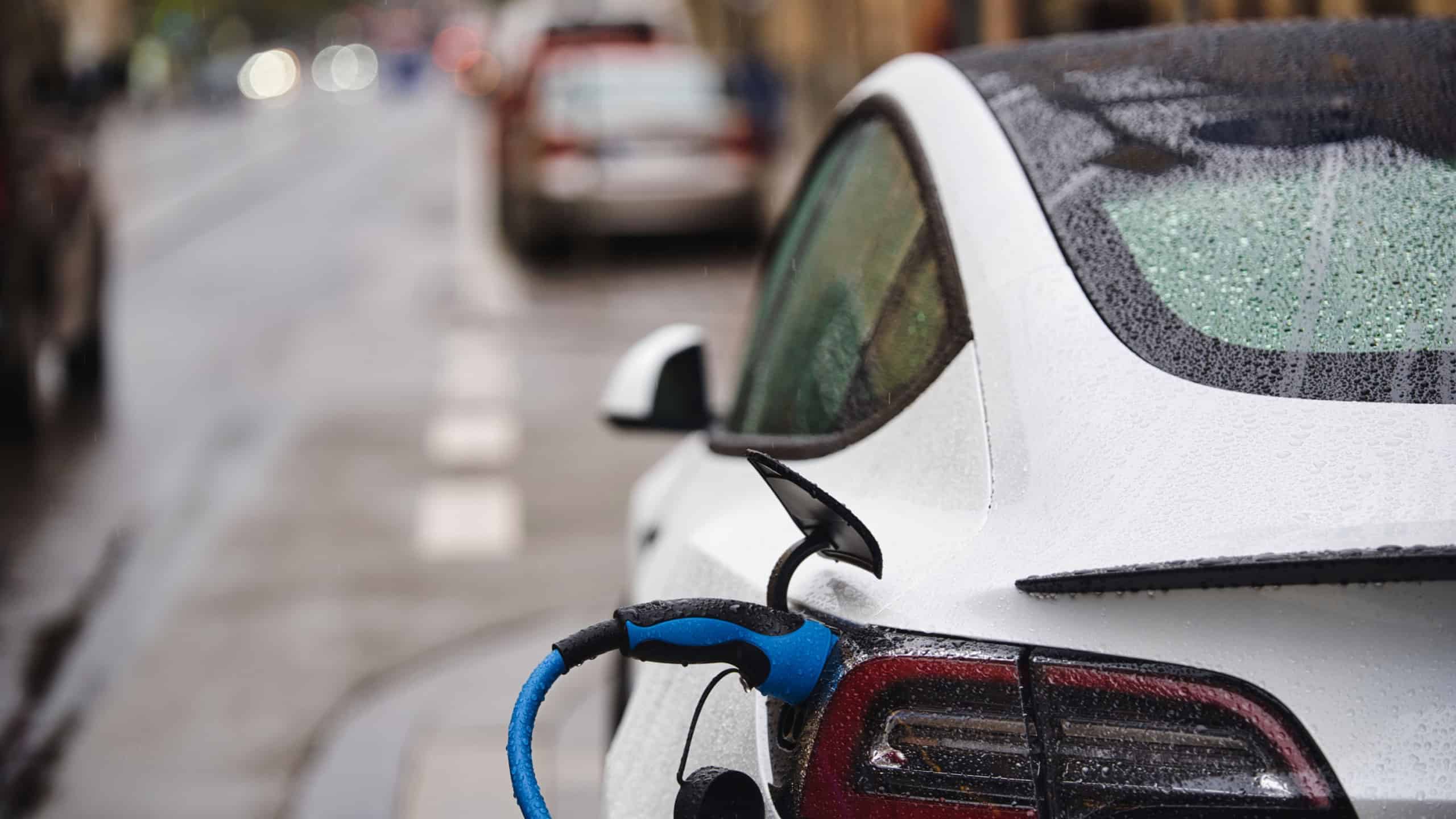 Electric car is connected to the charging station Electric vehicle standing in the rain