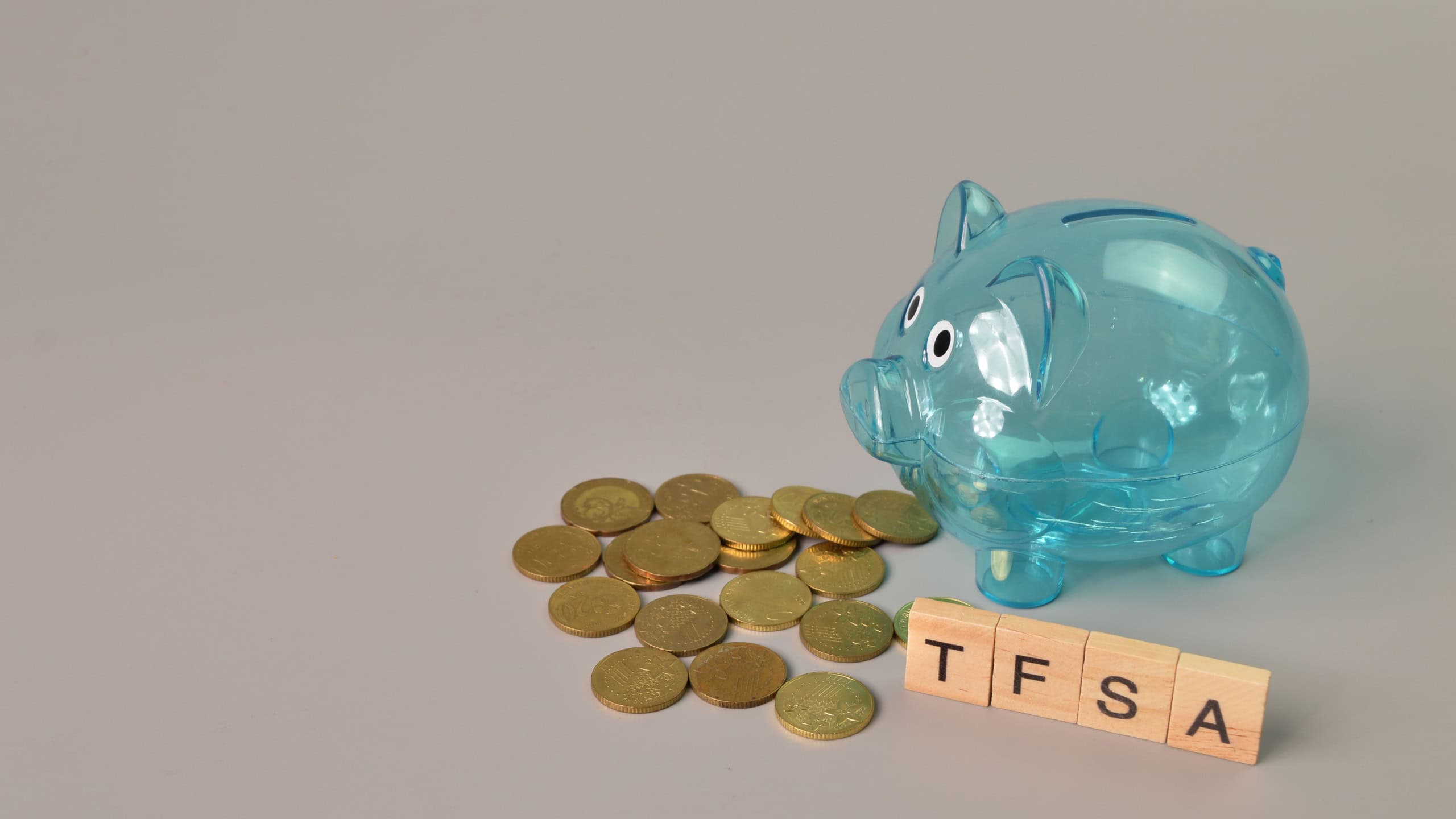 Piggy bank, stack of coins and wooden blocks with text TFSA stands for Tax-Free Savings Account
