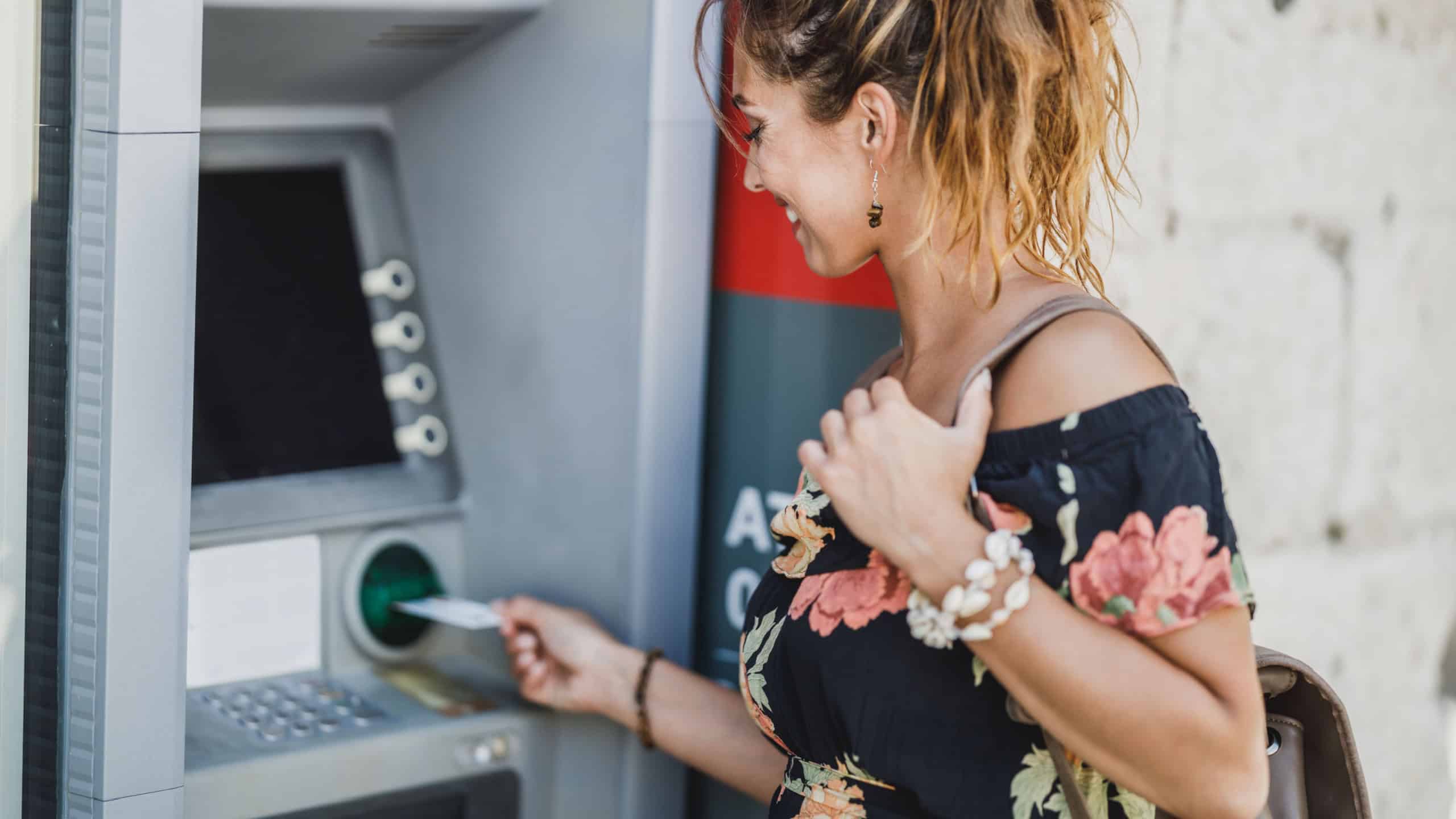 Side view of a woman inserting credit card and withdrawing cash at ATM machine.