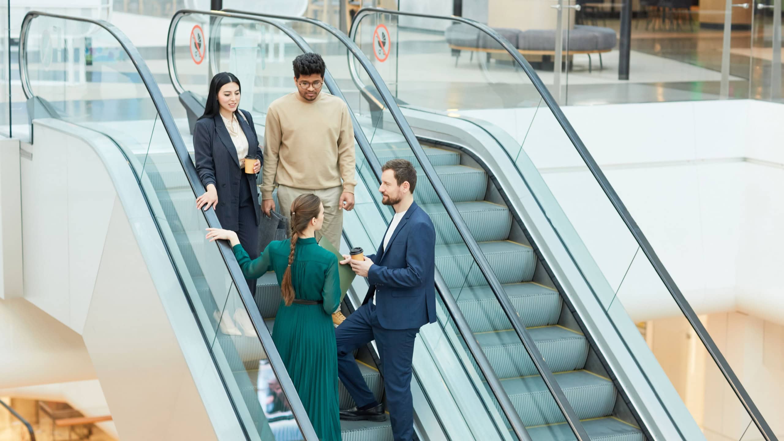 Wide angle view at group of business people standing on escalator in office building and communicating, copy space