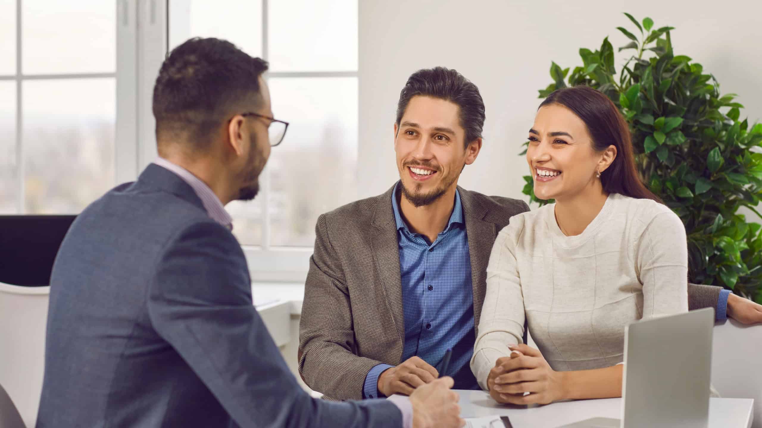 Young family couple meeting with real estate agent or loan broker. Happy, smiling man and woman sitting at office desk with realtor, business advisor or loan manager