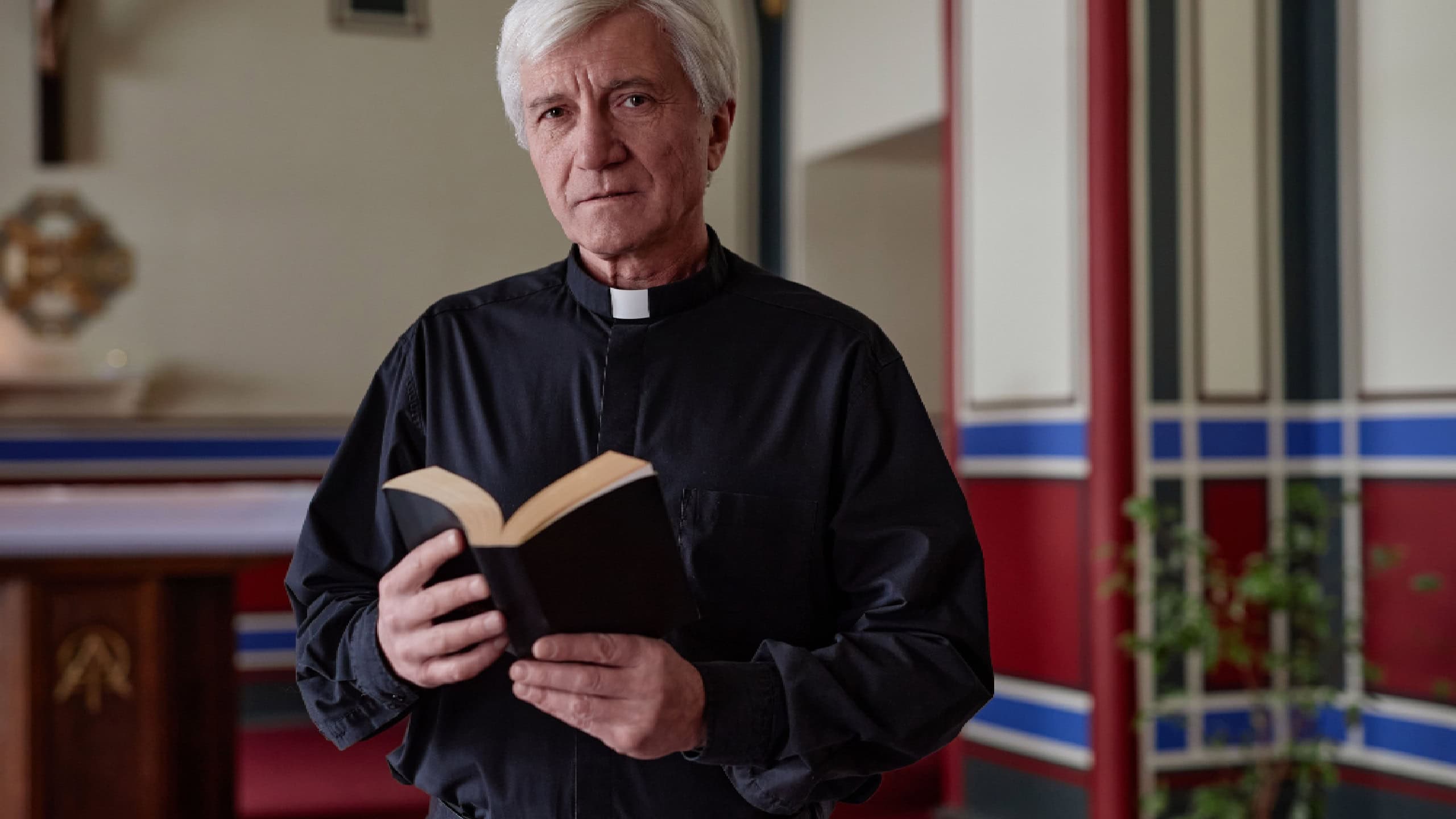 Portrait of senior priest looking at camera while standing with BIble book in church