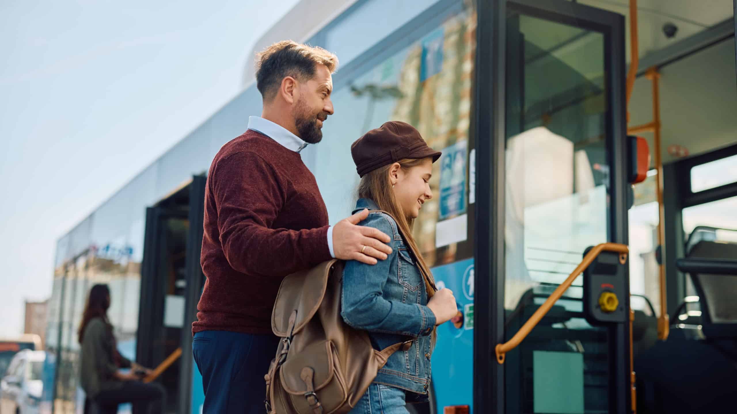 Happy little girl and her father boarding in a bus at the station.