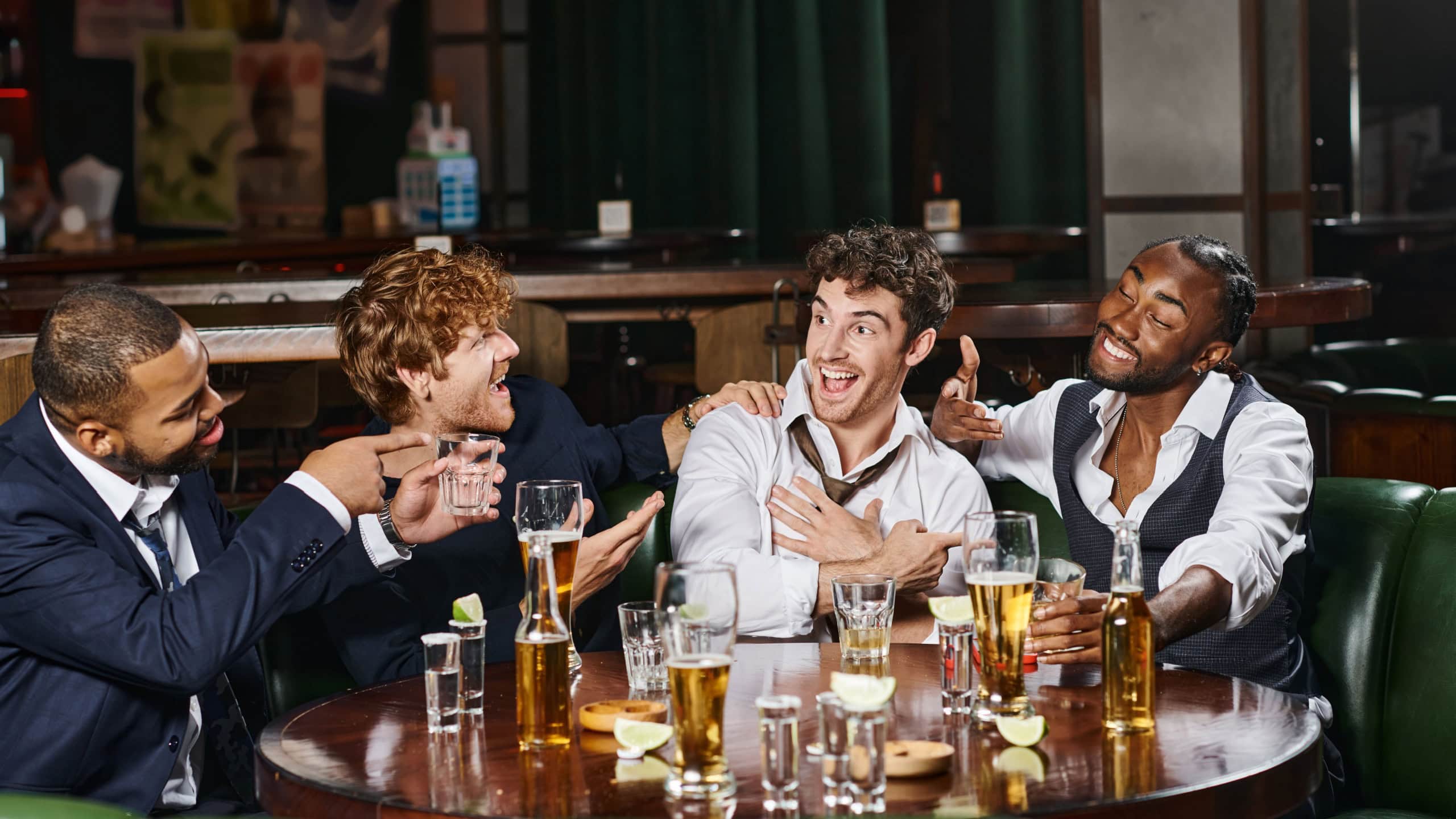 Happy multiethnic men pointing at friend in bar, male friends during bachelor party in bar