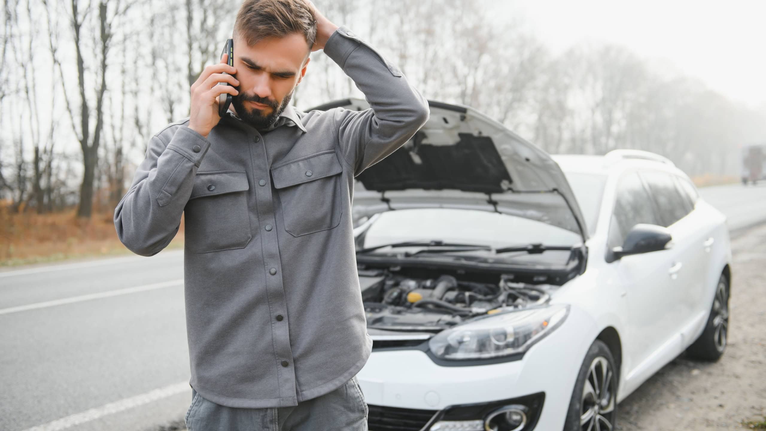 Sad driver holding his head having engine problem standing near broken car on the road. Car breakdown concept.