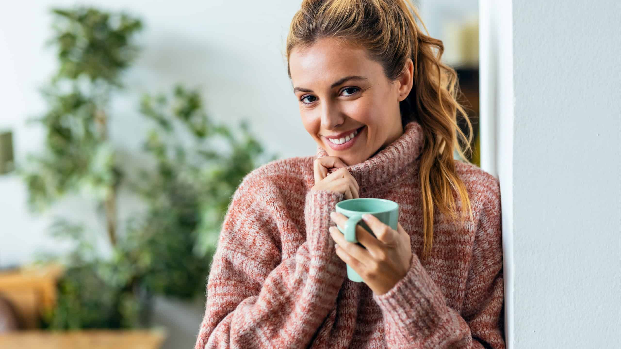 Shot of beautiful young woman drinking a hot cup of coffee while looking at camera in living room at home.