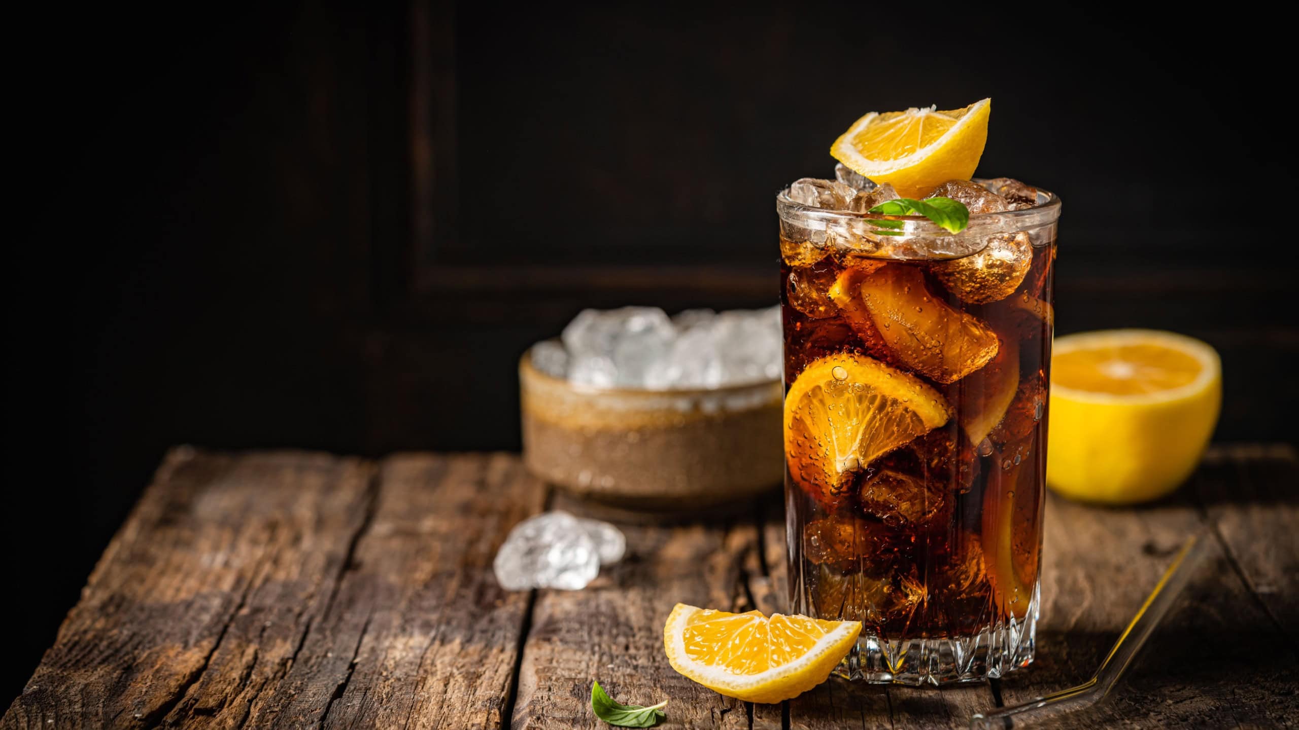 Cuba Libre in a glass with brown rum, cola, mint and lemon on dark background. Cuba Libre or long island iced tea cocktail with strong drinks