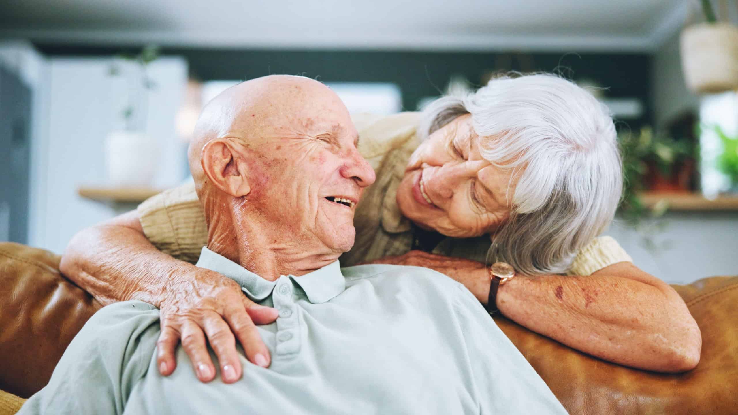 Senior couple, hug and love on sofa with happy marriage, support and conversation of retirement home. Elderly woman talking to man on couch for commitment, health and wellness with trust and security