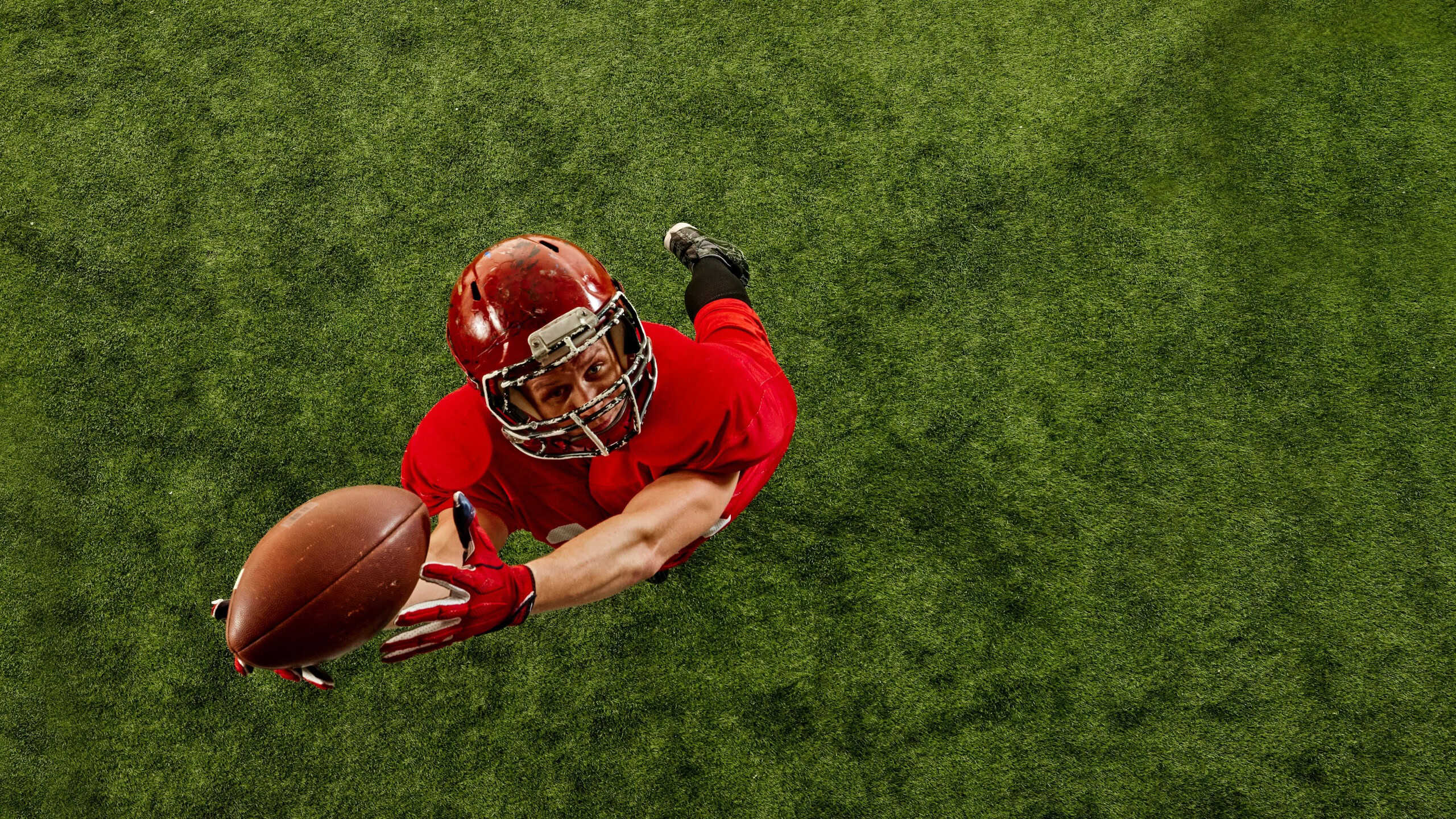 Top view image of concentrated man, American football player in red uniform in motion on stadium, catching ball with precision. Concept of sport, competition, tournament, game. Copy space