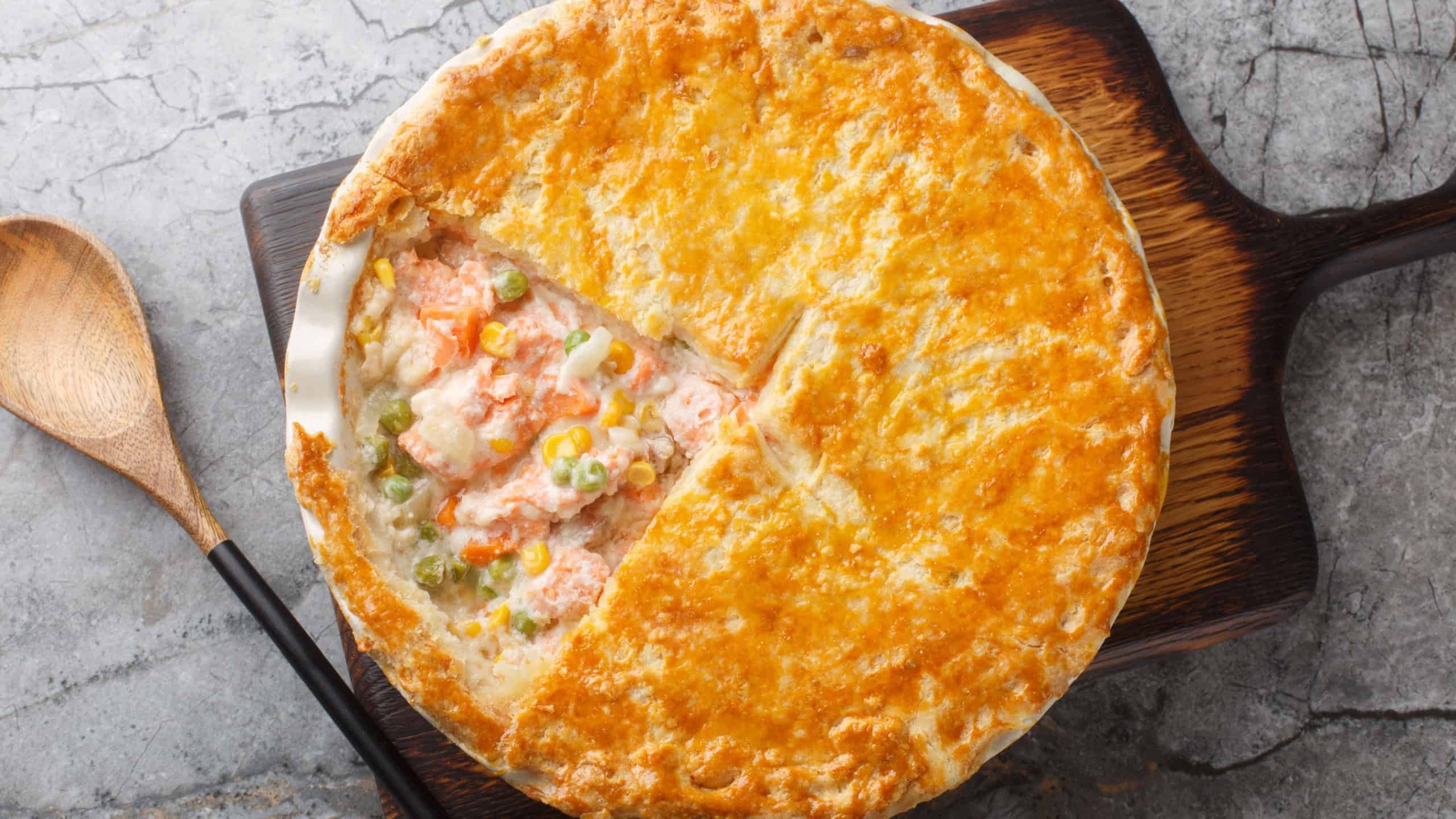 Homemade Salmon Pot Pie with carrots, corn, onion and peas and in a buttery pie crust closeup on the baking dish on the table.