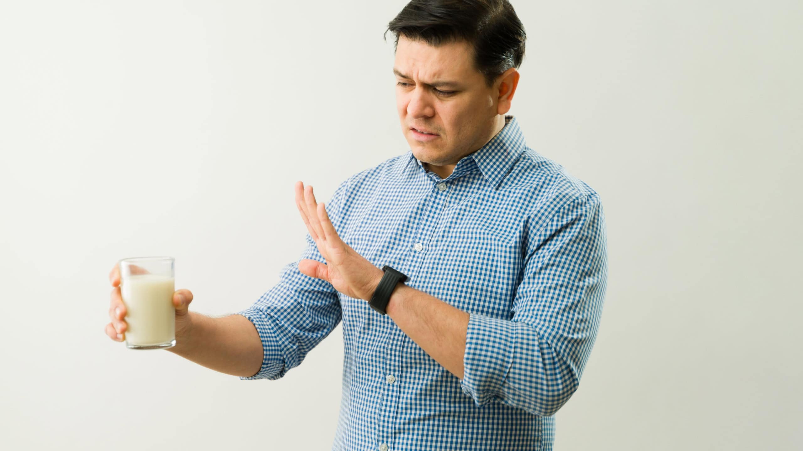 Latin man showing disgust for milk expressing lactose intolerance symptoms and problems with dairy products