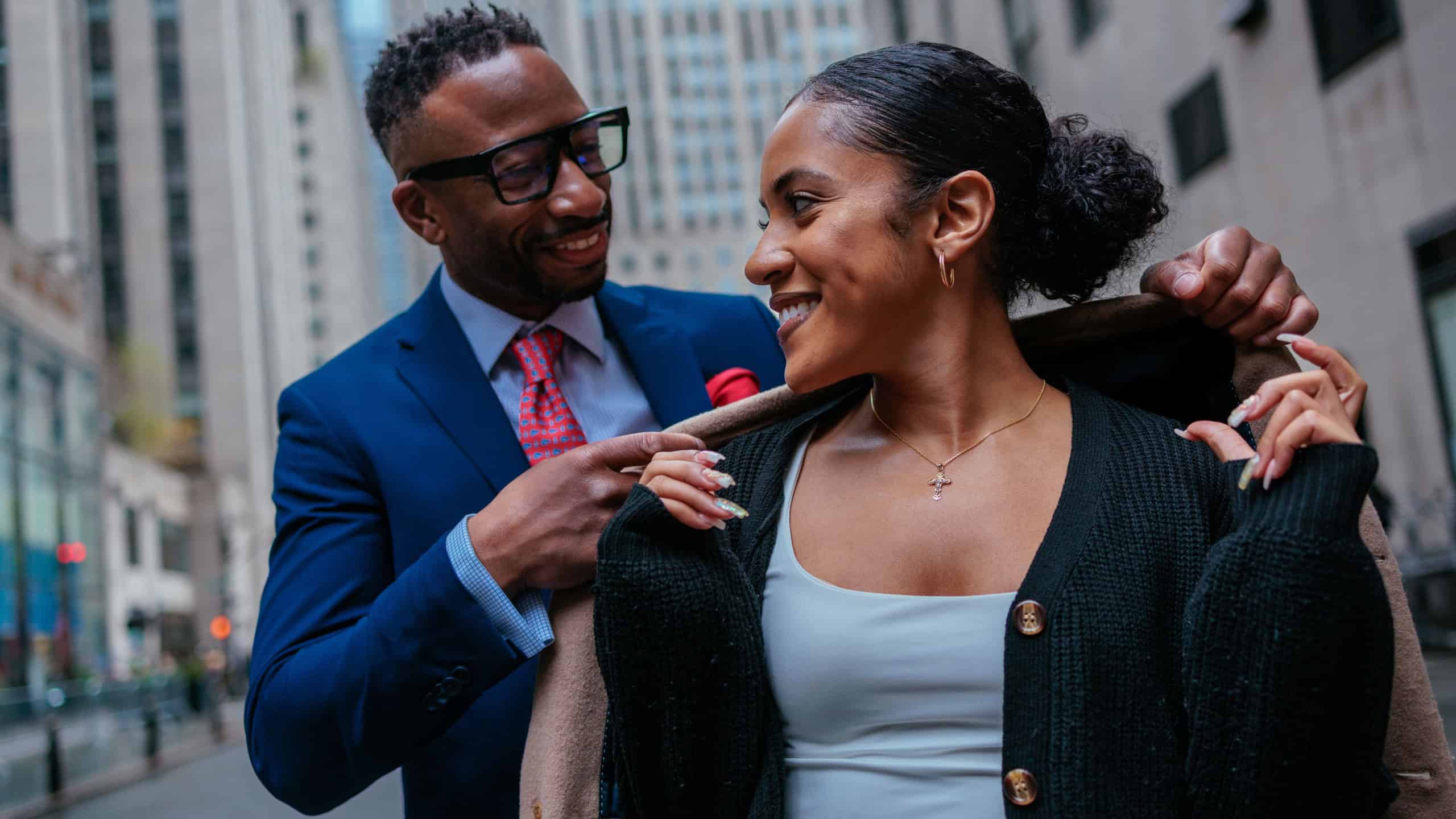 A stylish couple dressed in chic outerwear stands confidently on a Manhattan street, amid the iconic sights of New York City