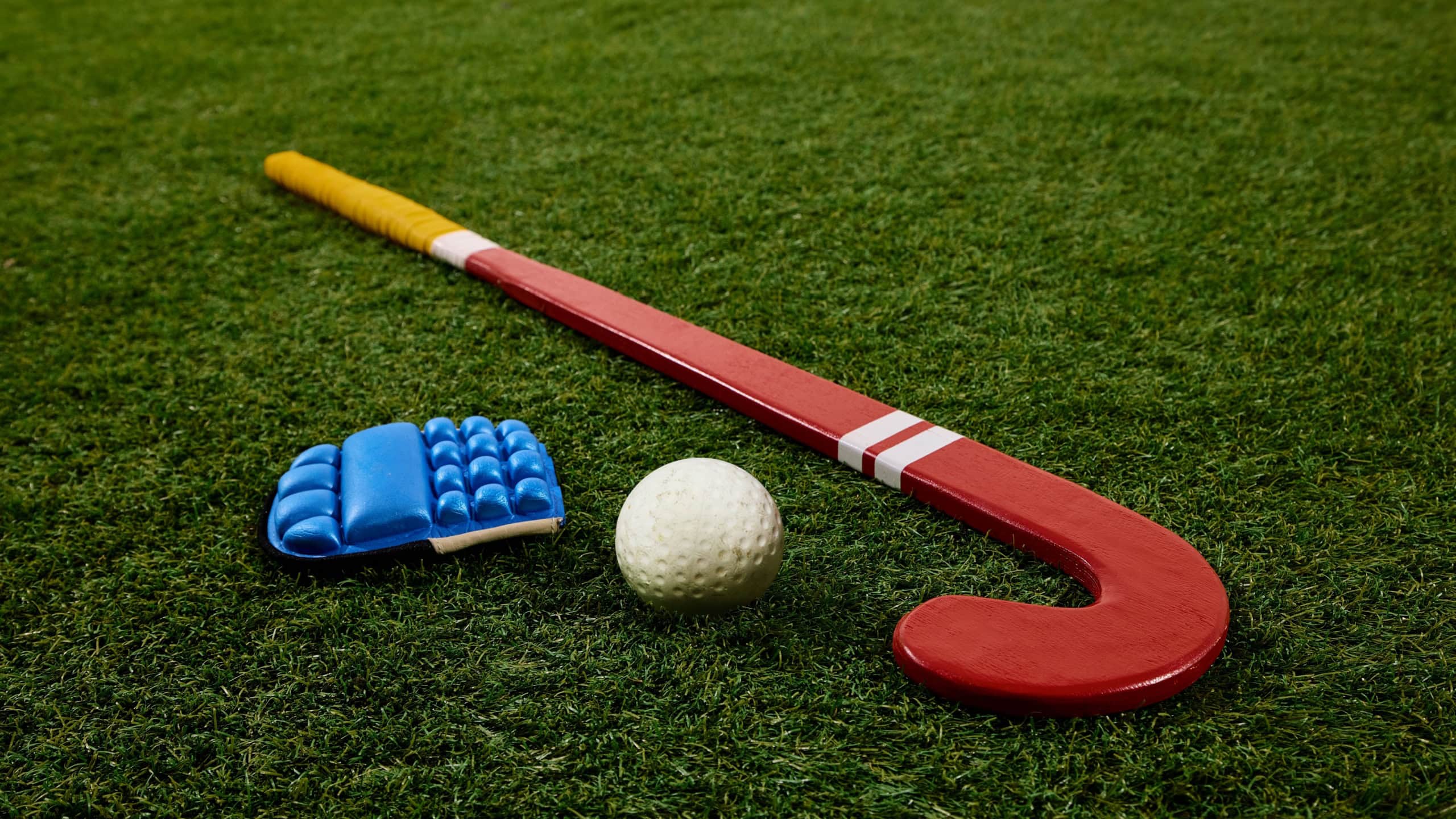 Close-up of essential field hockey equipment, glove, ball, and stick, carefully placed on green grass field against white studio background. Concept of sport events, competition, championship, game
