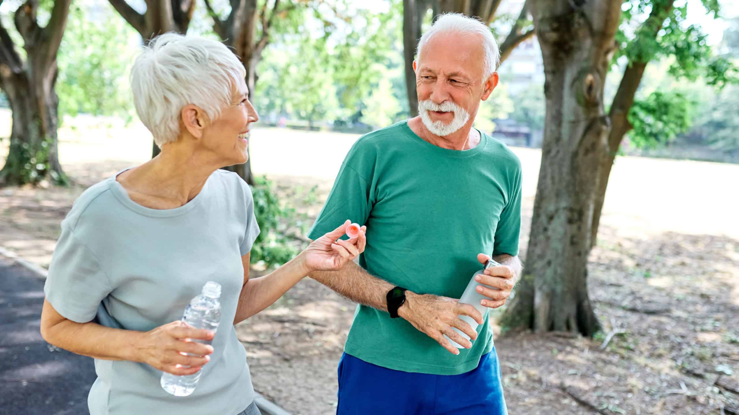 Smiling active senior couple jogging exercising and having fun and laughing together taking and walking a break in the park