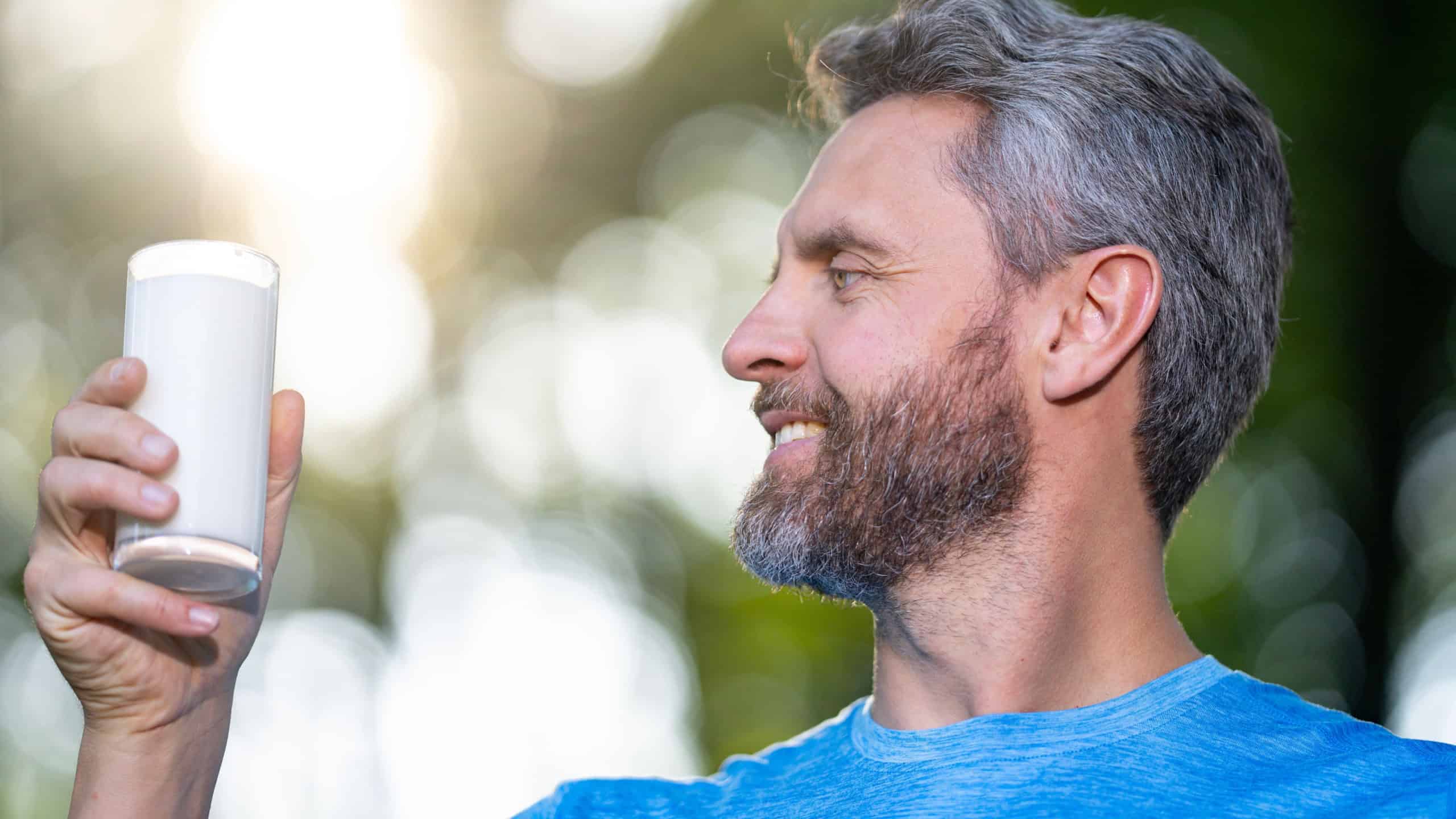 A healthy man holds a glass of fresh milk outdoors. Organic milk as a natural supplement after a workout. Sport man drink glass of milk. A man holds a fresh milk shake as part of a healthy diet.