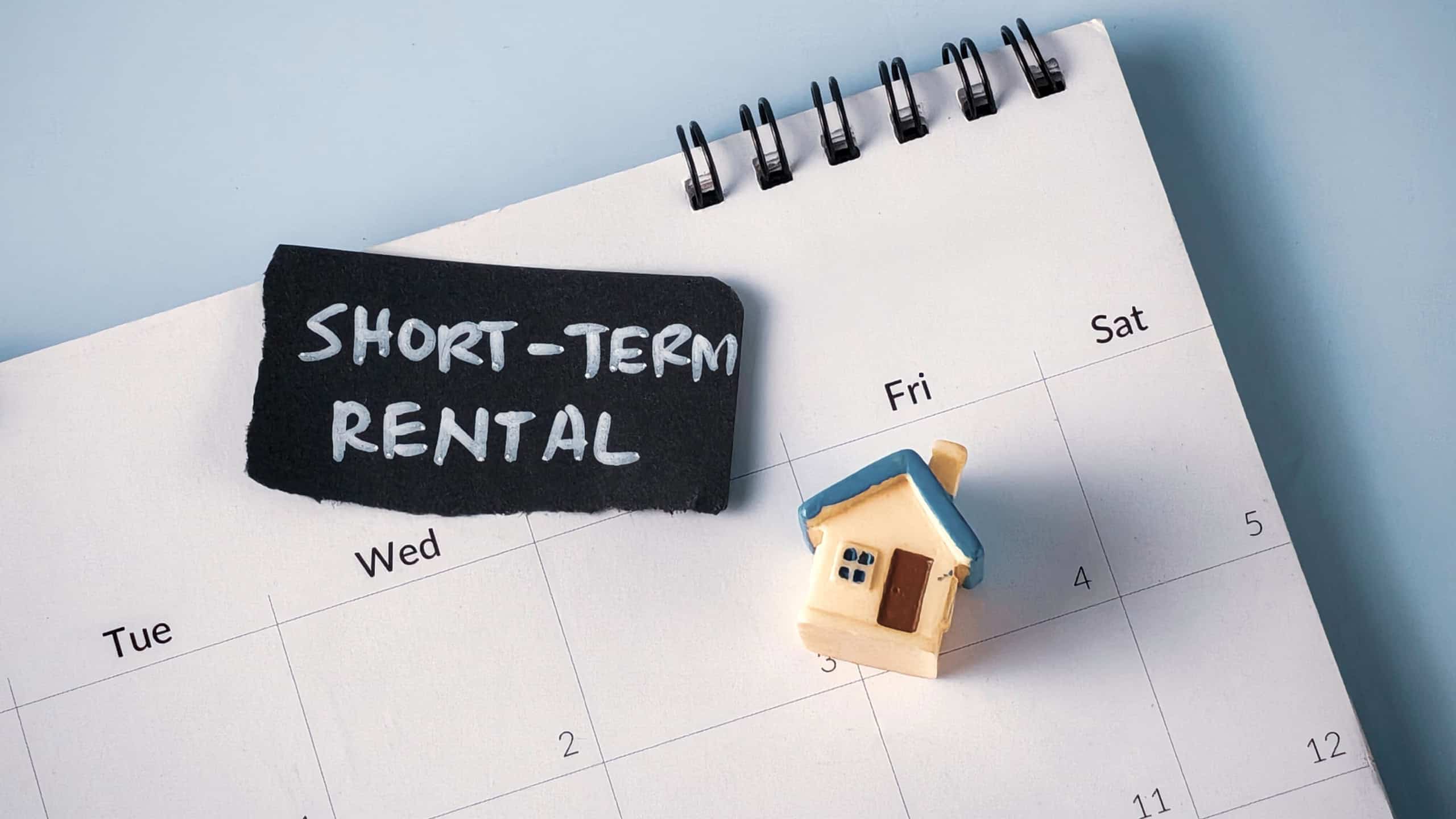 Miniature House on Calendar with "Short-Term Rental" Text: Concept for Vacation Property, Travel Planning, and Airbnb Strategy