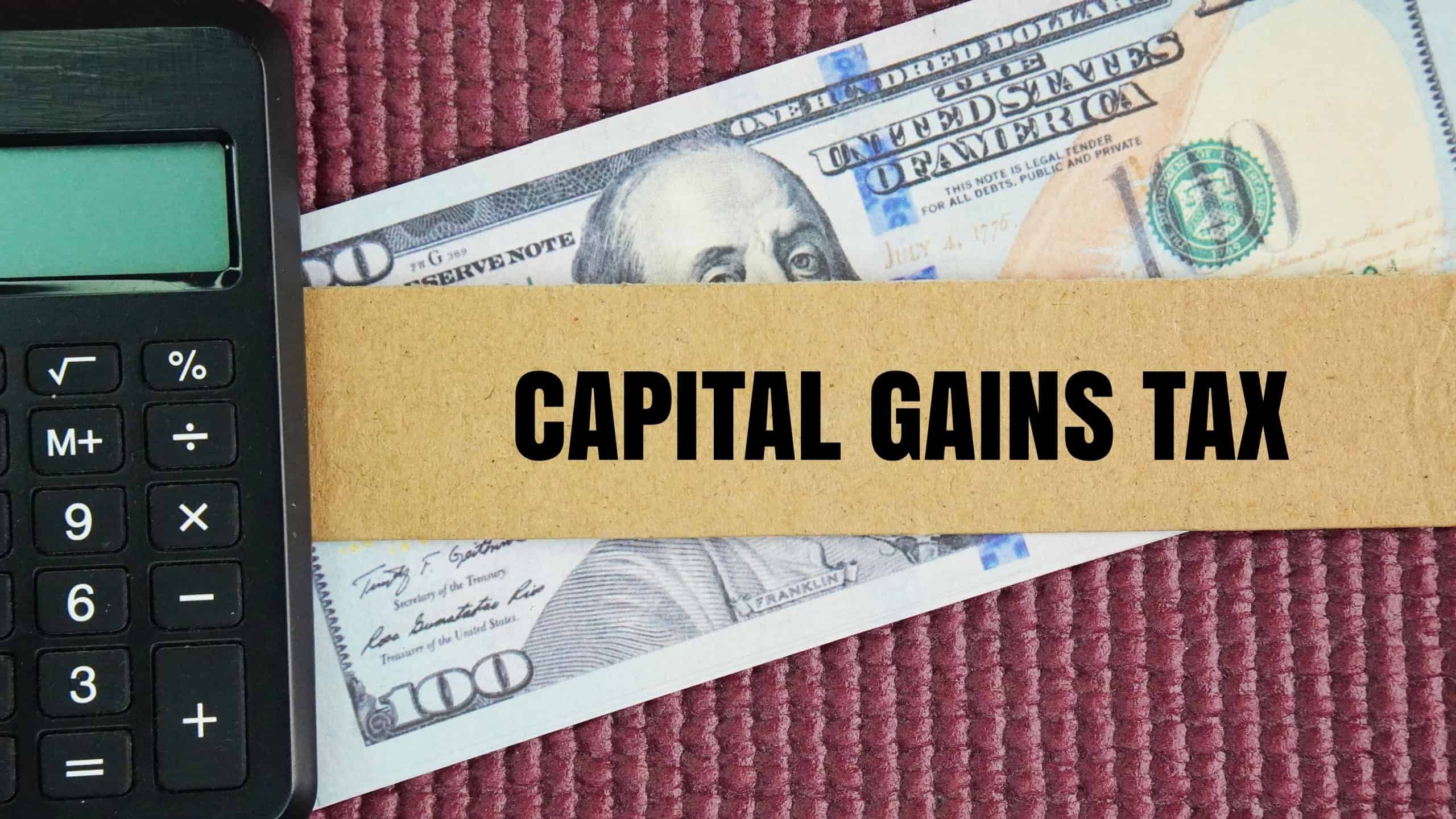 Calculator and paper money with the word CAPITAL GAINS TAX. the concept of profit tax payment. Business concept. Mandatory gratuitous payment is established