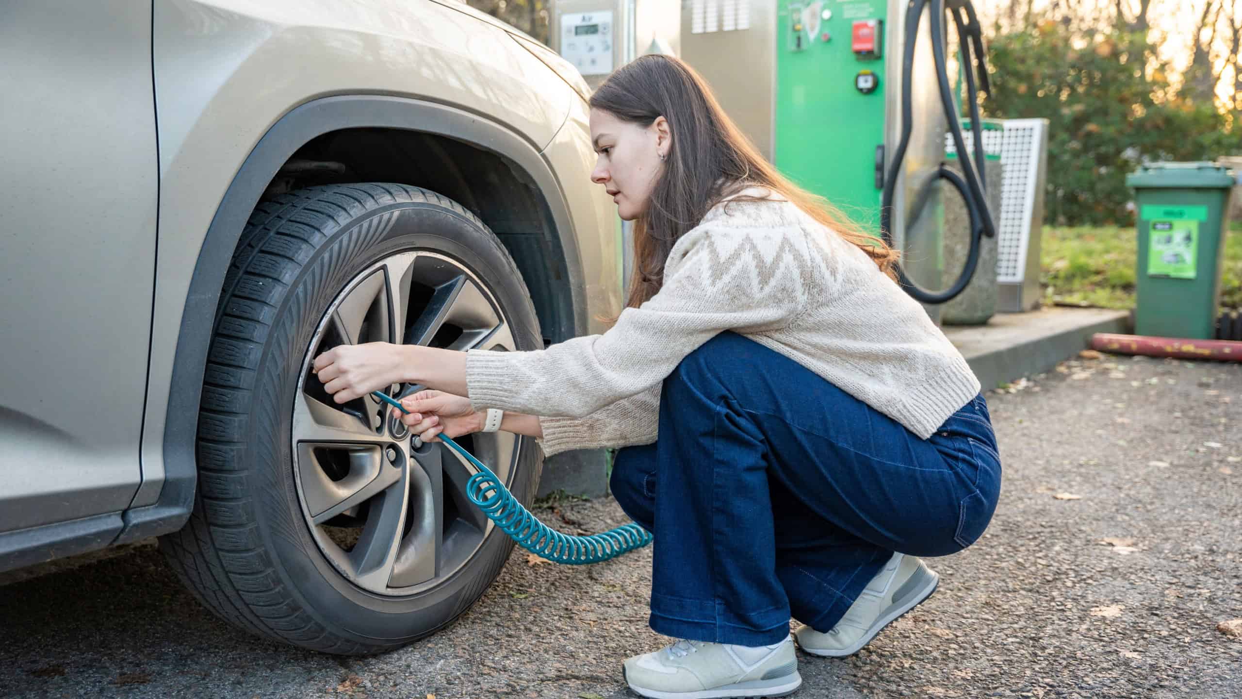 Female driver inflating a tire with air at a public gas station. Auto care and safety.