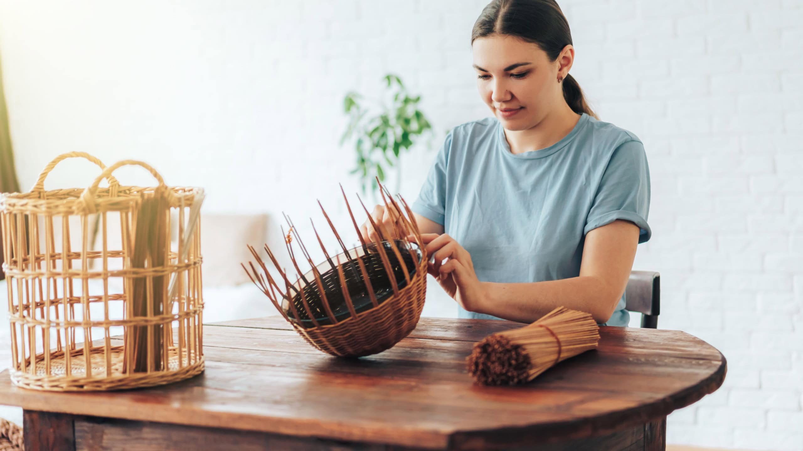 Woman weaves basket of paper tubes on wooden table.