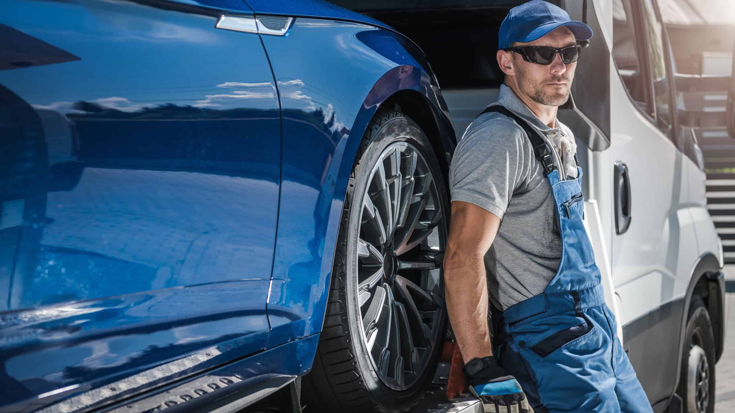 Caucasian Towing Truck Driver in His 40s Staying Next to His Vehicle. Repossessed Car on the Truck.
