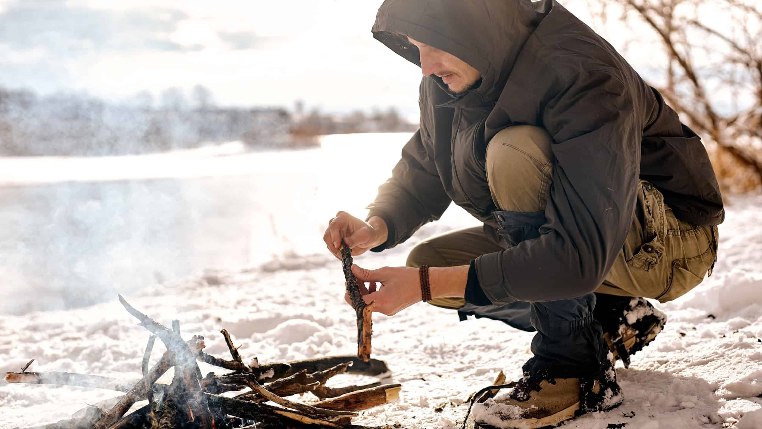 young man on expedition, making fire in forest, wild nature. bonfire by male person. fire made of wood. bushcraft, adventure, travel, tourism and camping concept. extreme condition