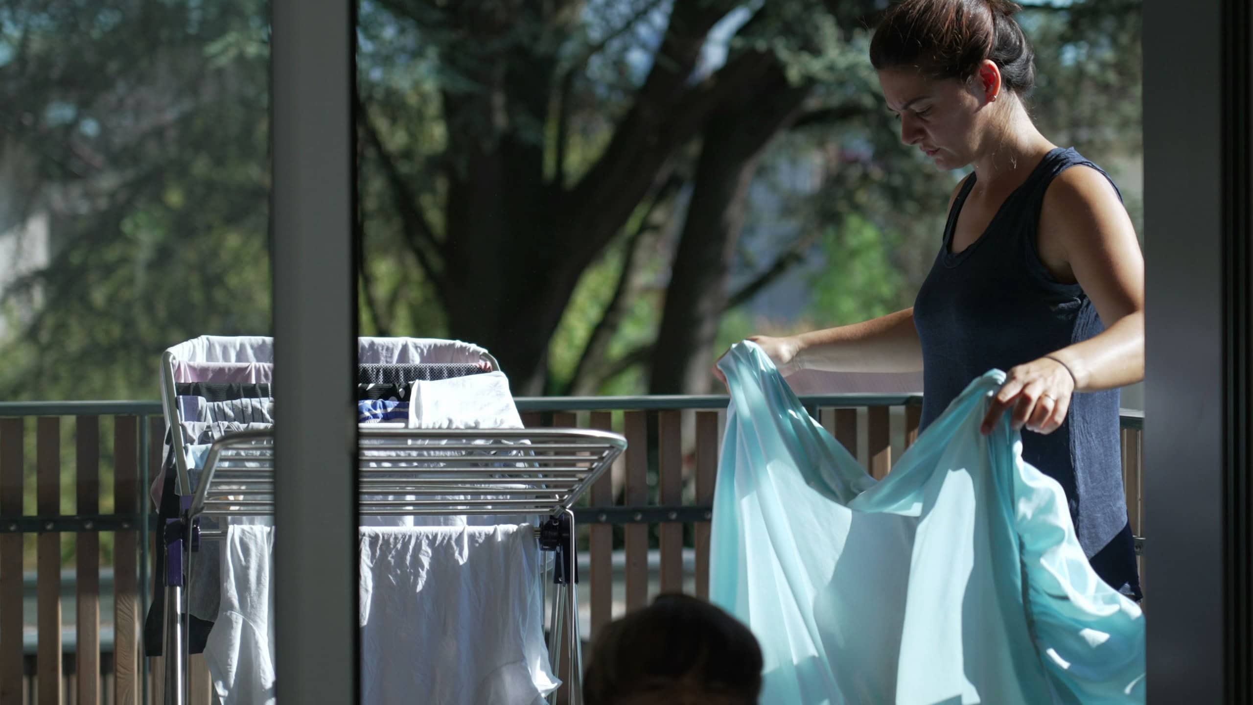 Serious housewife hangs wet clothes on dryer after laundry at apartment balcony. Household chores and housekeeping