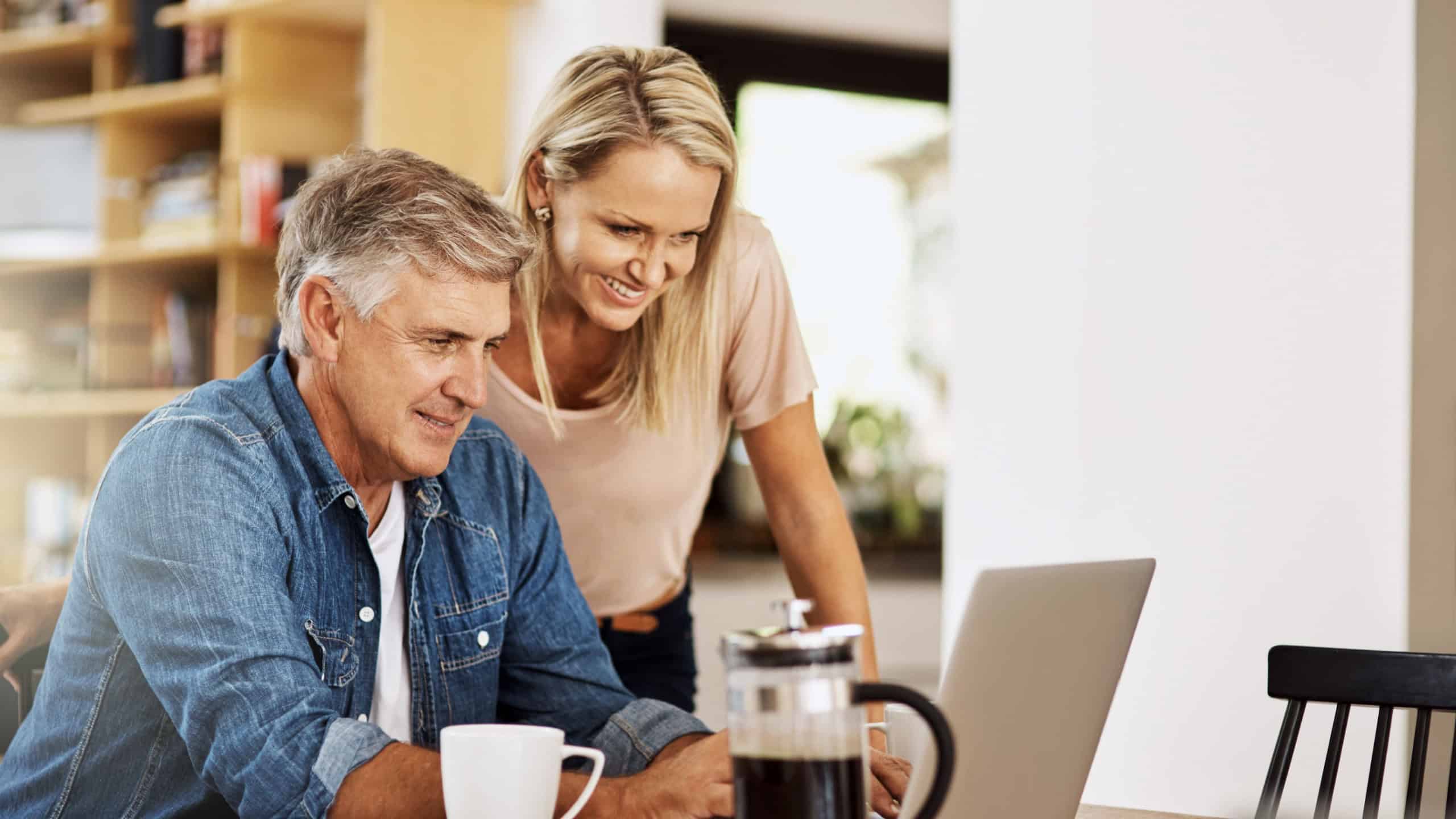 Happy couple, laptop and life insurance research at home with happiness and computer. Email, online banking and reading of a woman and man together in a house planning finance budget for retirement