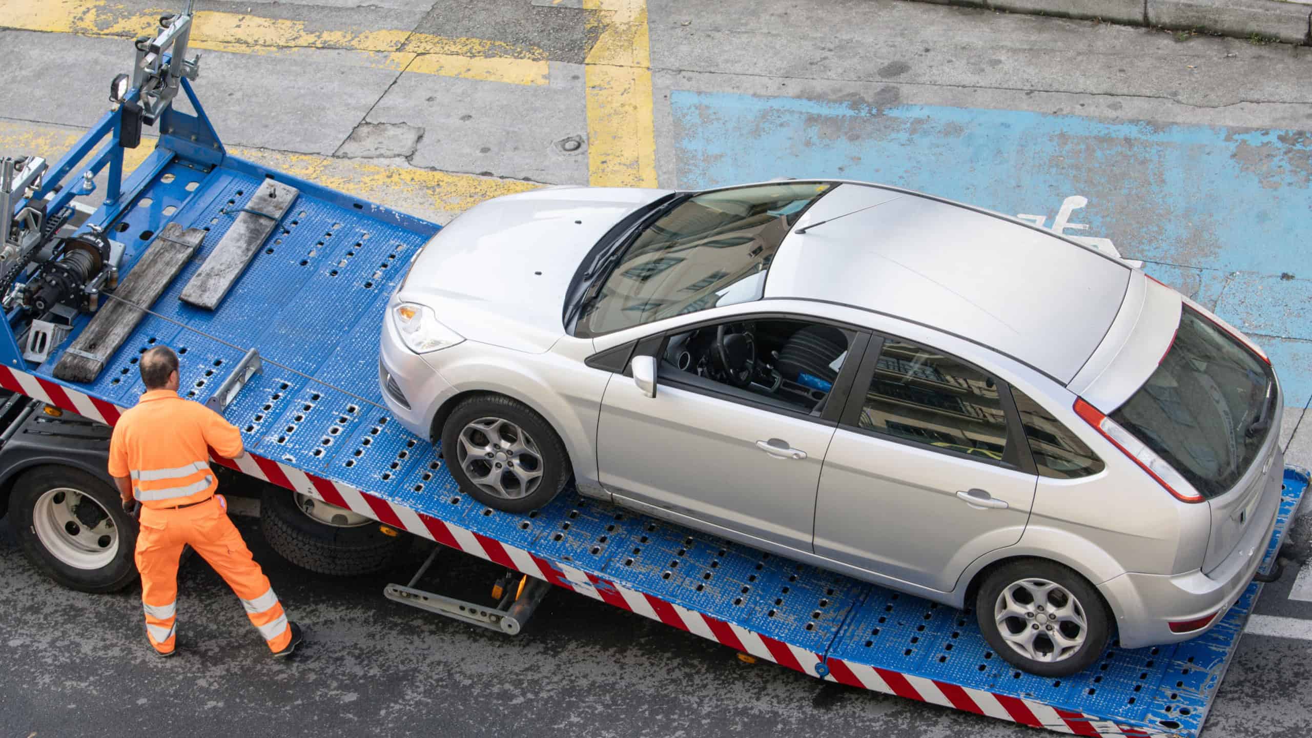 Galicia, Spain; july 08, 2023: Roadside assistance worker raising a car on tow truck. Towing service on the city
