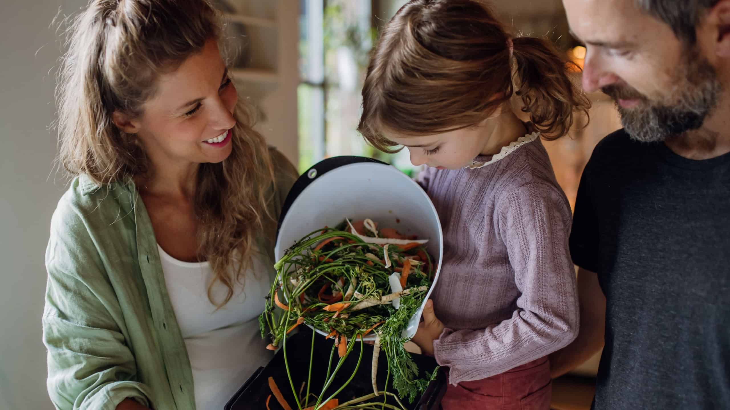 Girl helping parents put kitchen waste, peel and leftover vegetables scraps into kitchen compostable waste. Concept of composting kitchen biodegradable waste.