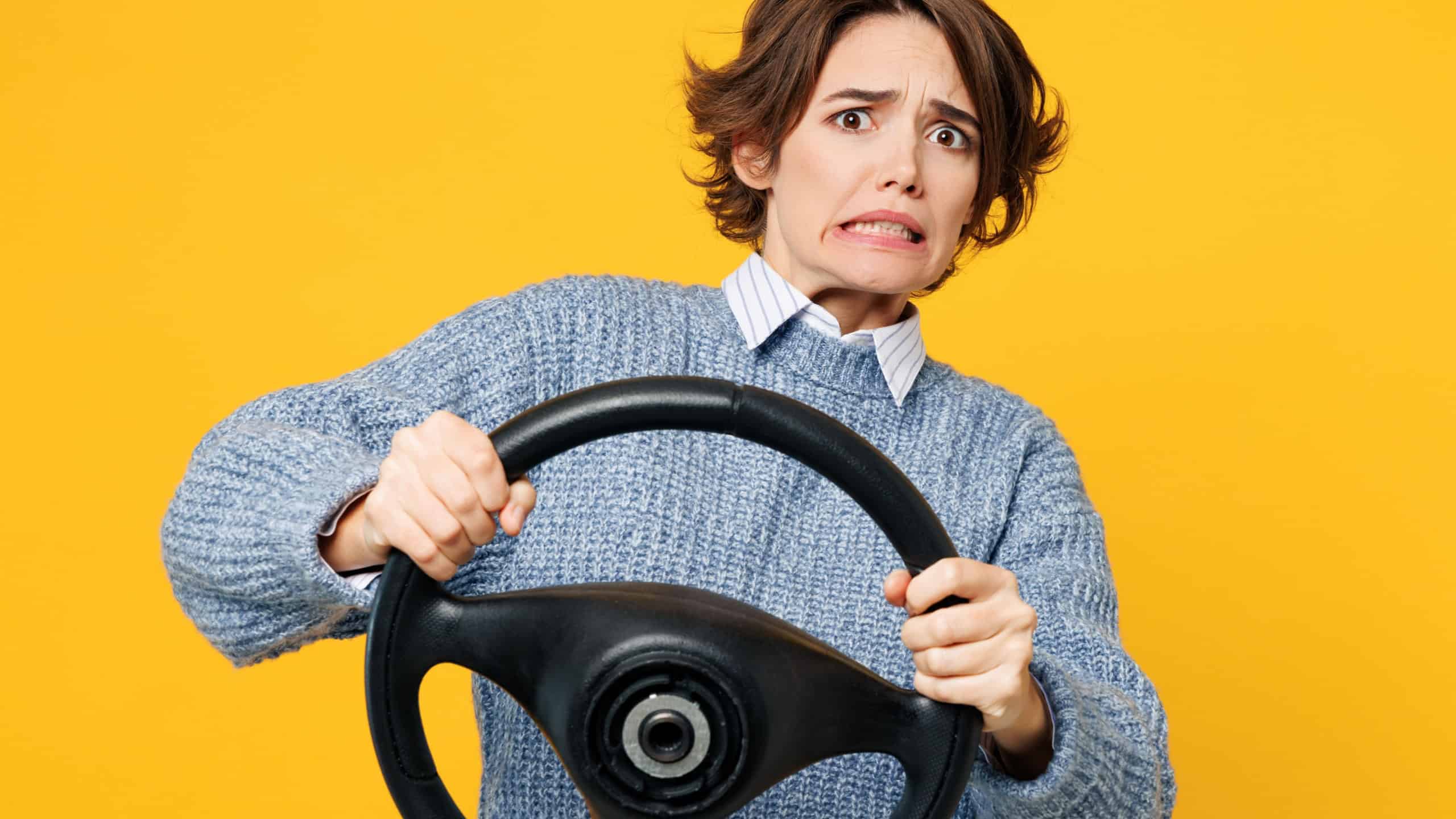 Young sad scared astonished woman she wears grey knitted sweater shirt casual clothes hold steering wheel driving car look camera isolated on plain yellow background studio portrait. Lifestyle concept
