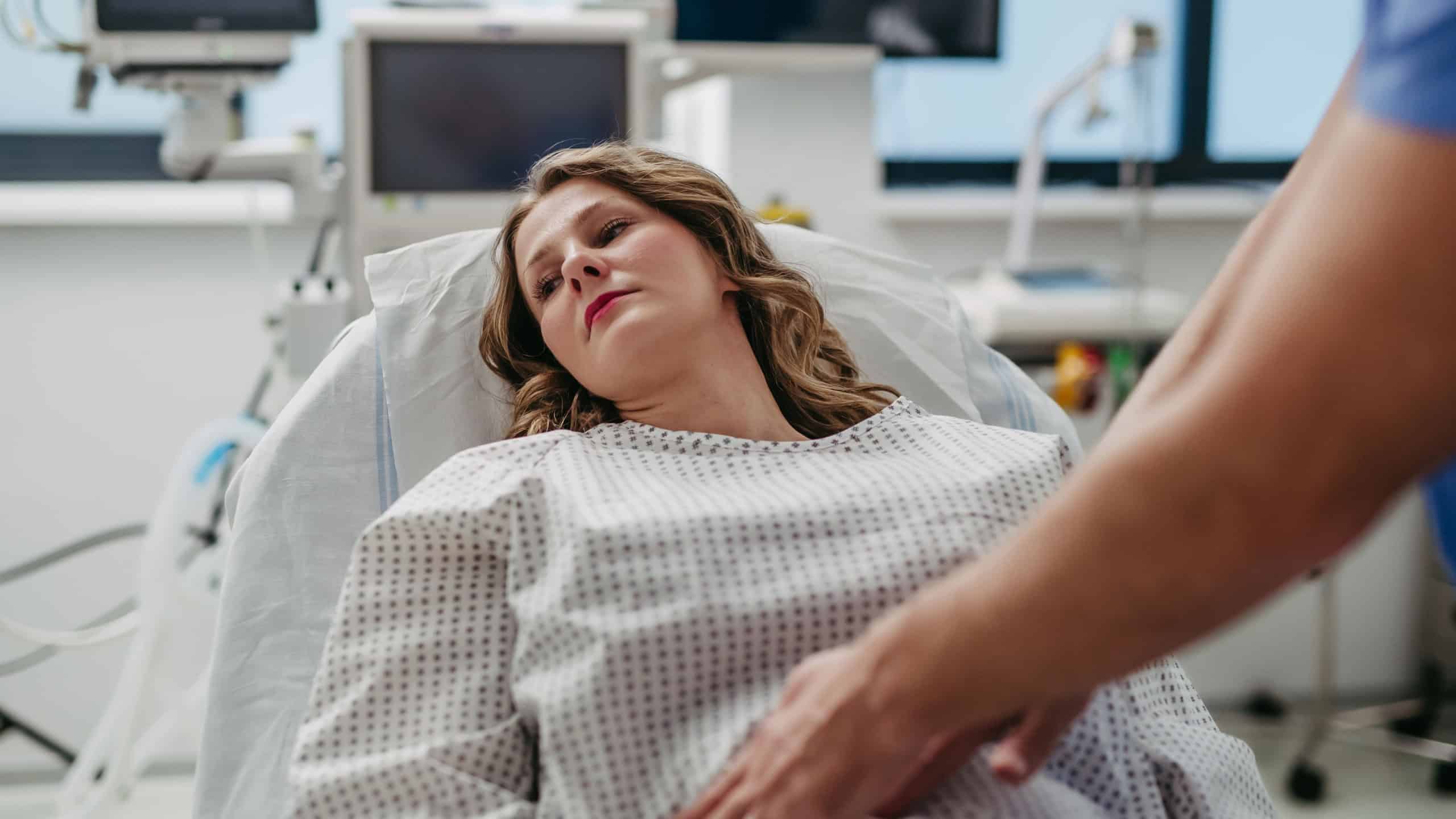 Doctor palpating woman's abdomen, using hands and steady pressure.