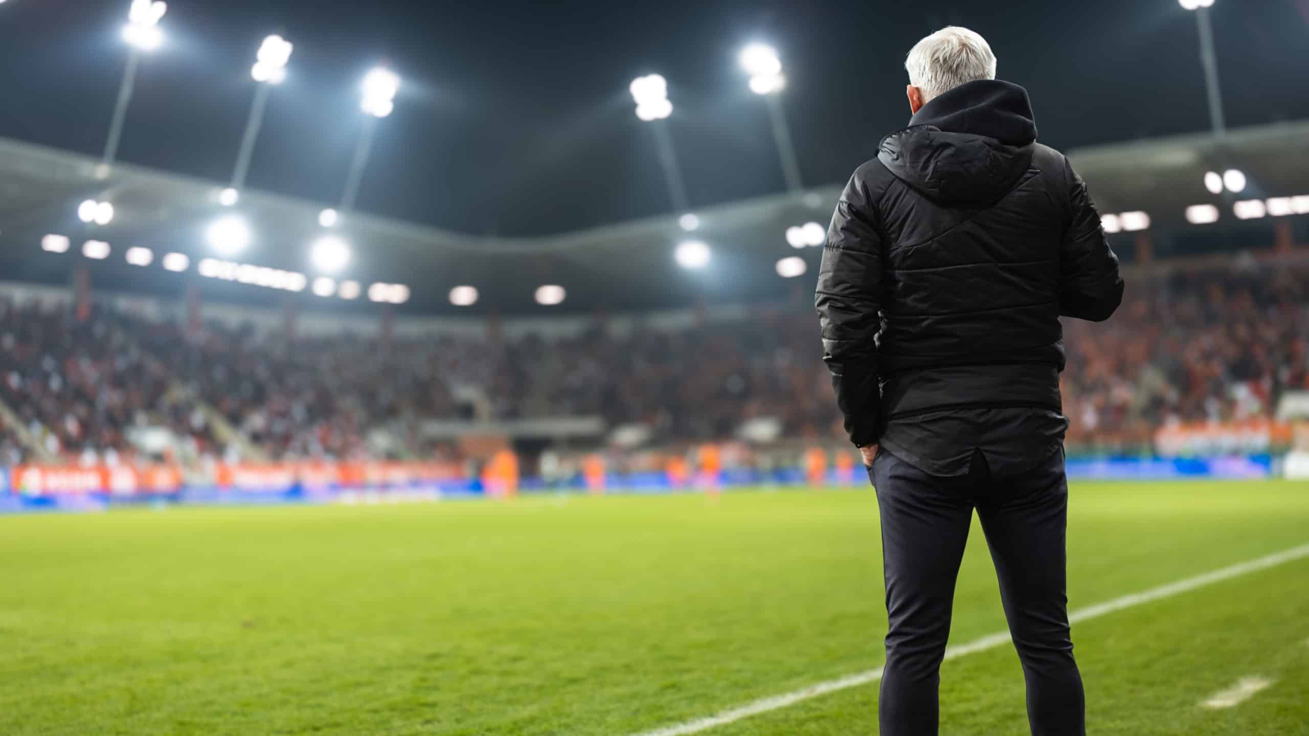 Head coach's back and soccer match at the stadium in the background.