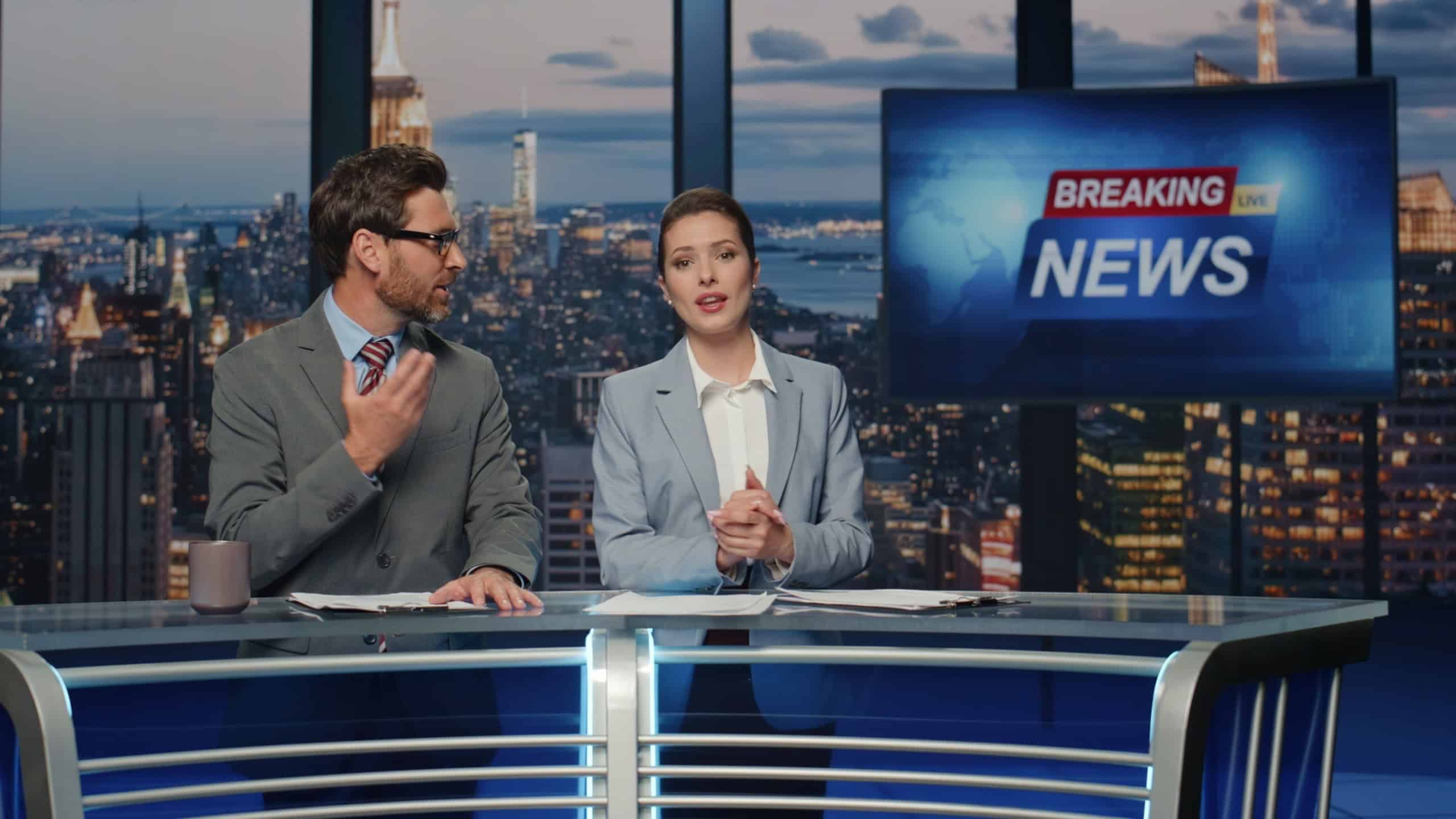 Emotional news readers discussing live tv newscast in night media studio closeup. Positive charismatic presenters smiling communicating with audience. Cheerful couple anchors talking daily reportage
