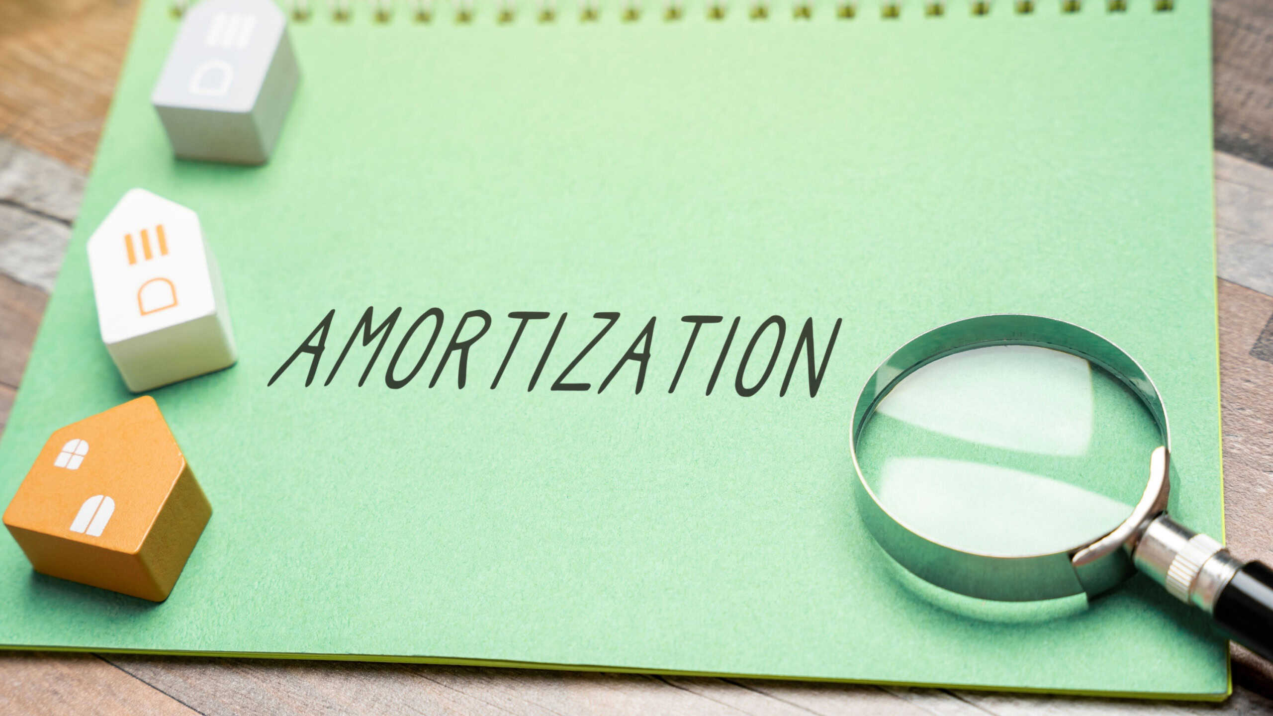The inscription Amortization in a notepad and miniature houses. Process of gradually paying off a mortgage through regular, scheduled payments. Real estate and finance concept