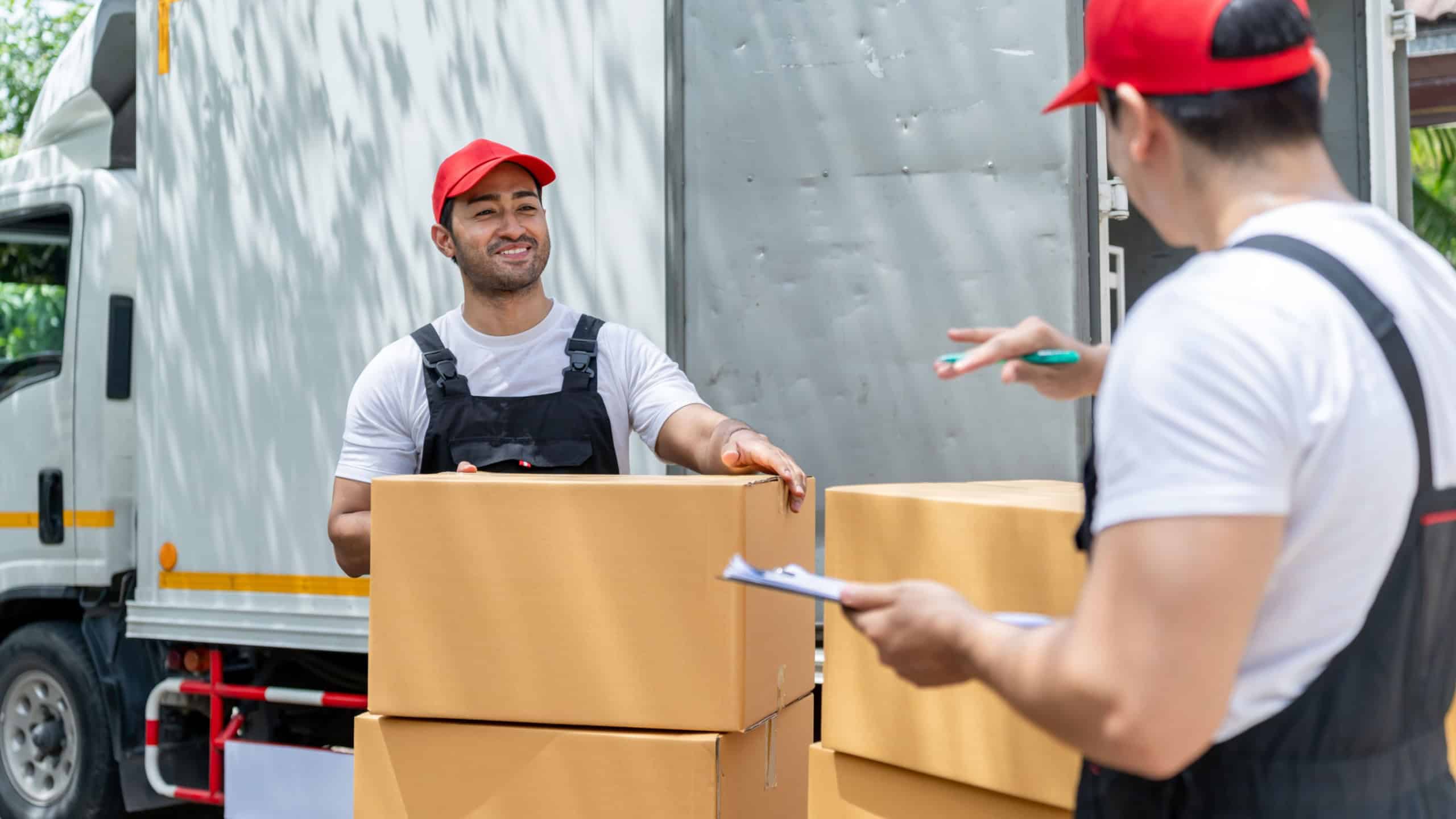 Caucasian delivery man checking a list of delivering package in truck. Attractive courier postman worker team in uniform working and preparing to load deliver box cardboard postal from car van.