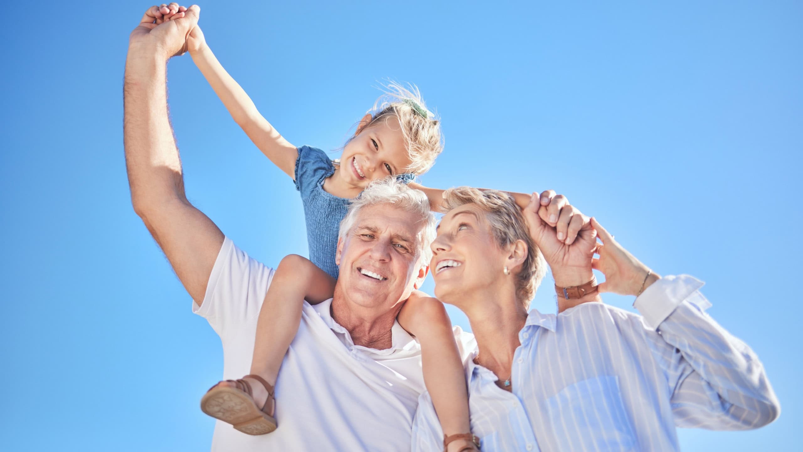 Portrait, girl and grandparents for summer vacation, family holiday and travel adventure. Happy child, blue sky and shoulder ride with smile, joy and tourism for childhood bonding and outdoors fun