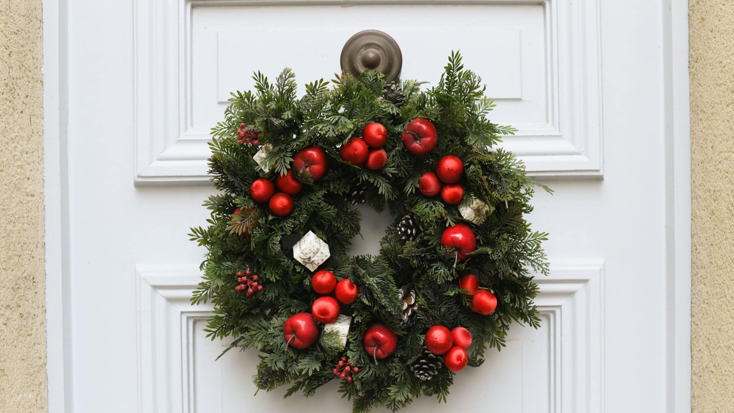 Christmas wreath with branches and red apples on a white door