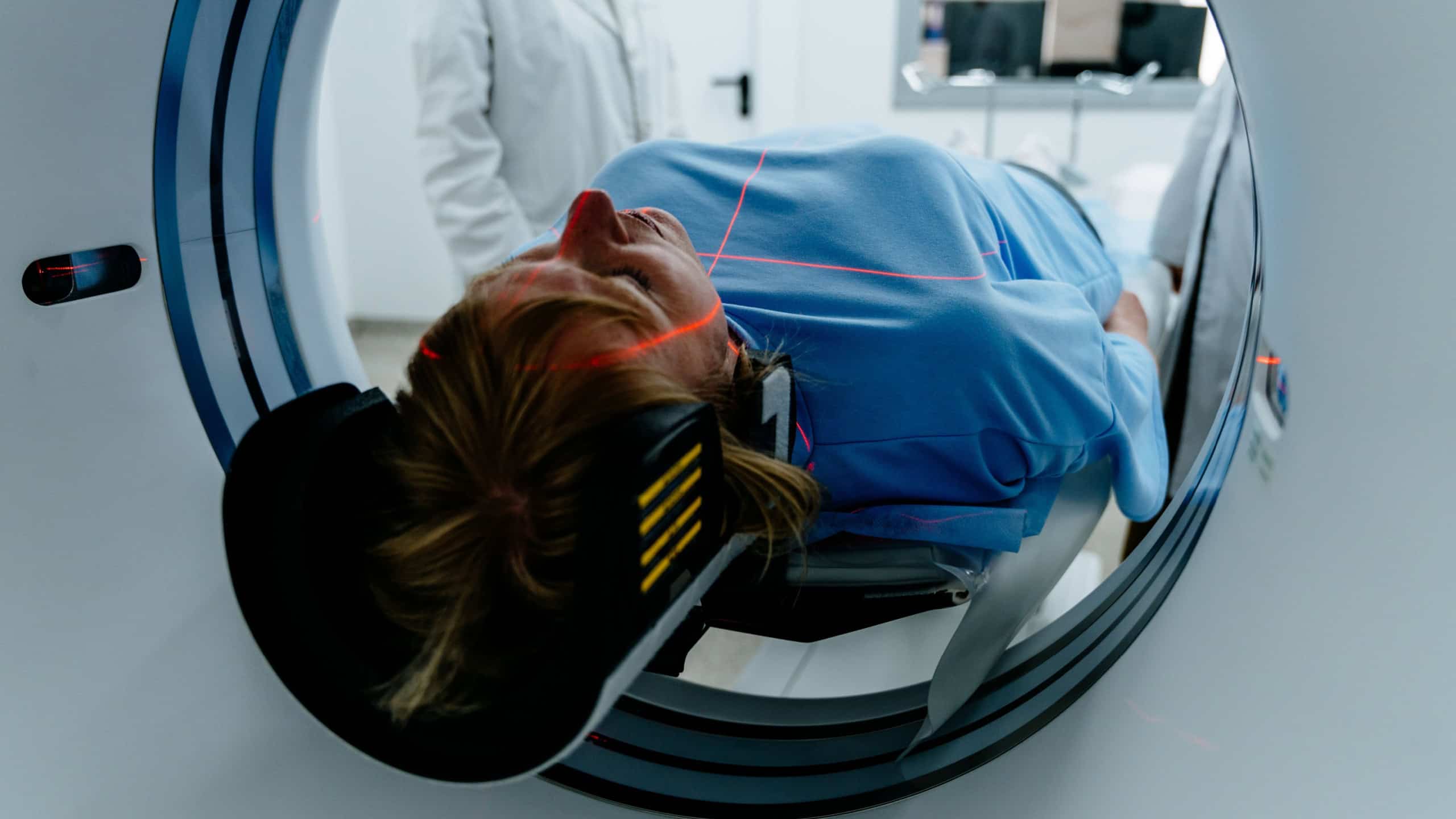 Mature female patient lying on table entering MRI machine in hospital setting. Medical professional in white coat standing nearby. Professionalism, precision, and modern health technology.