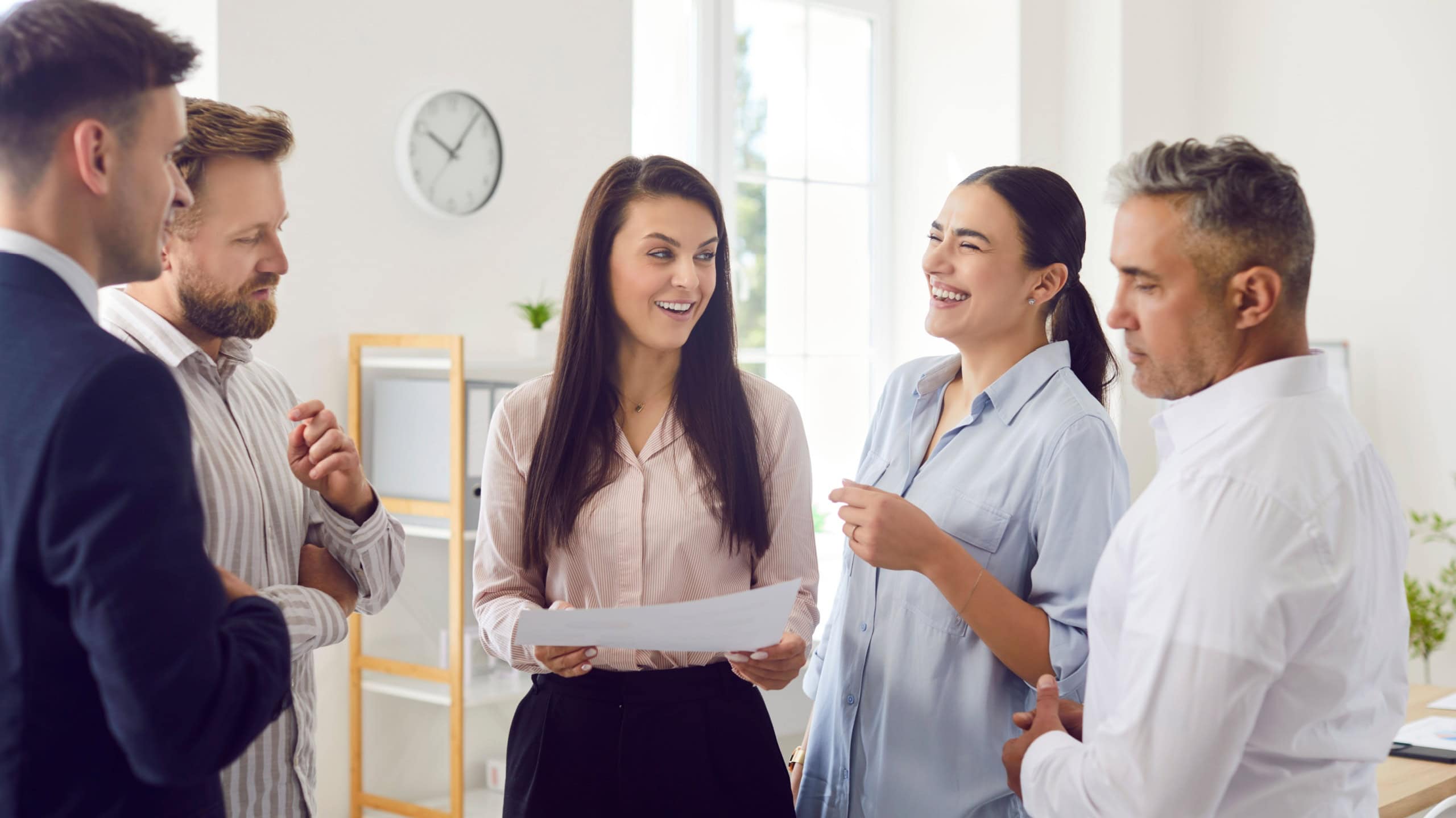 A group of office employees standing at their workplace communicating, close-up. Concept of division in a team. A man at a discussion does not agree with the majority opinion, awkwardness