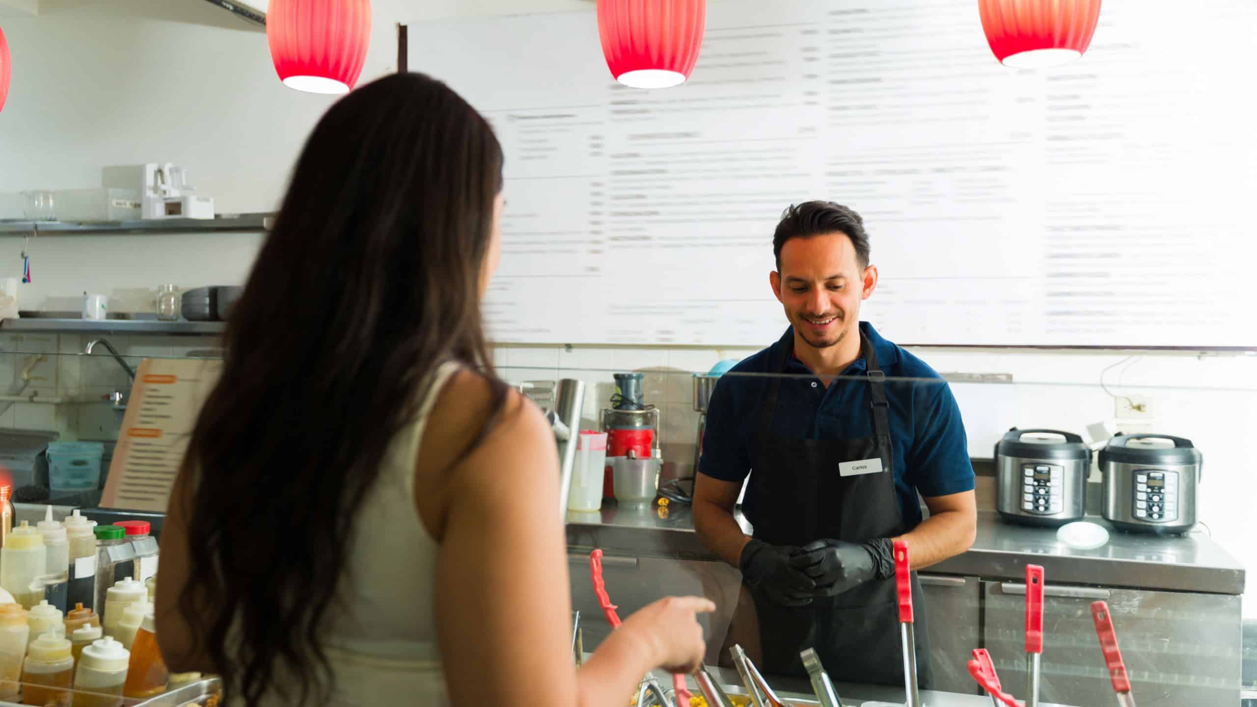 Latin restaurant employee wearing black gloves helping customer ordering fresh salad at salad bar