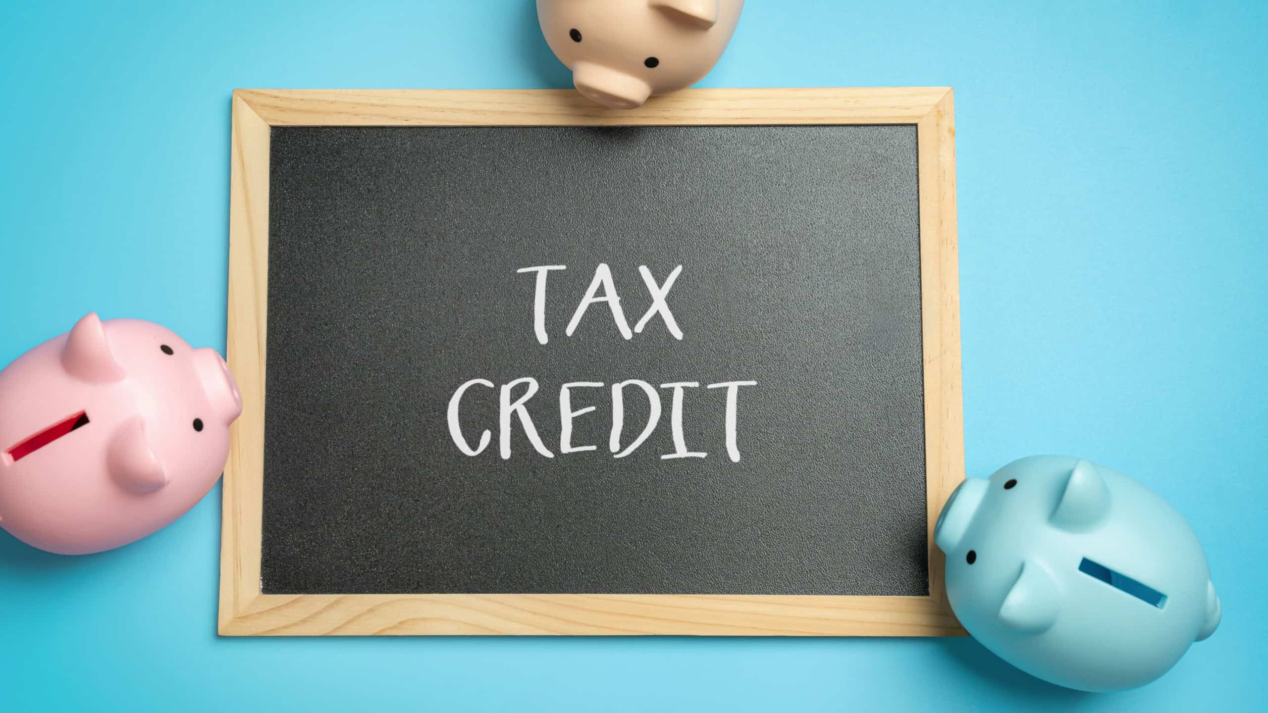 Tax credit concept. Amount that reduces the total tax owed, directly lowering the taxpayer’s tax bill. Board with inscription and piggy banks