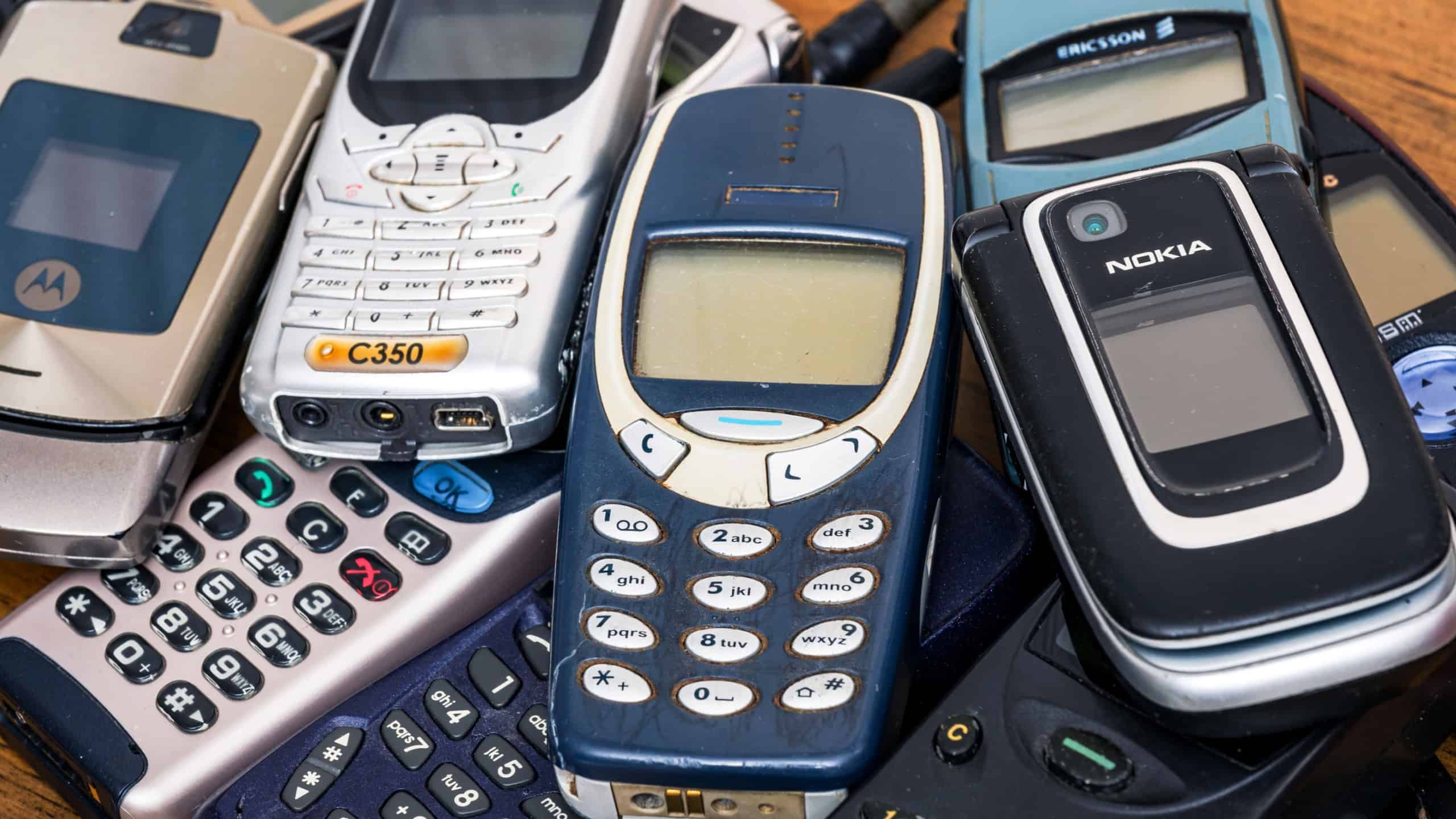 Milan, Lombardy, Italy - February 25, 2025: Old Nokia, Ericsson and Motorola cell phones stacked on a wooden table represent a milestone in the history of mobile communication