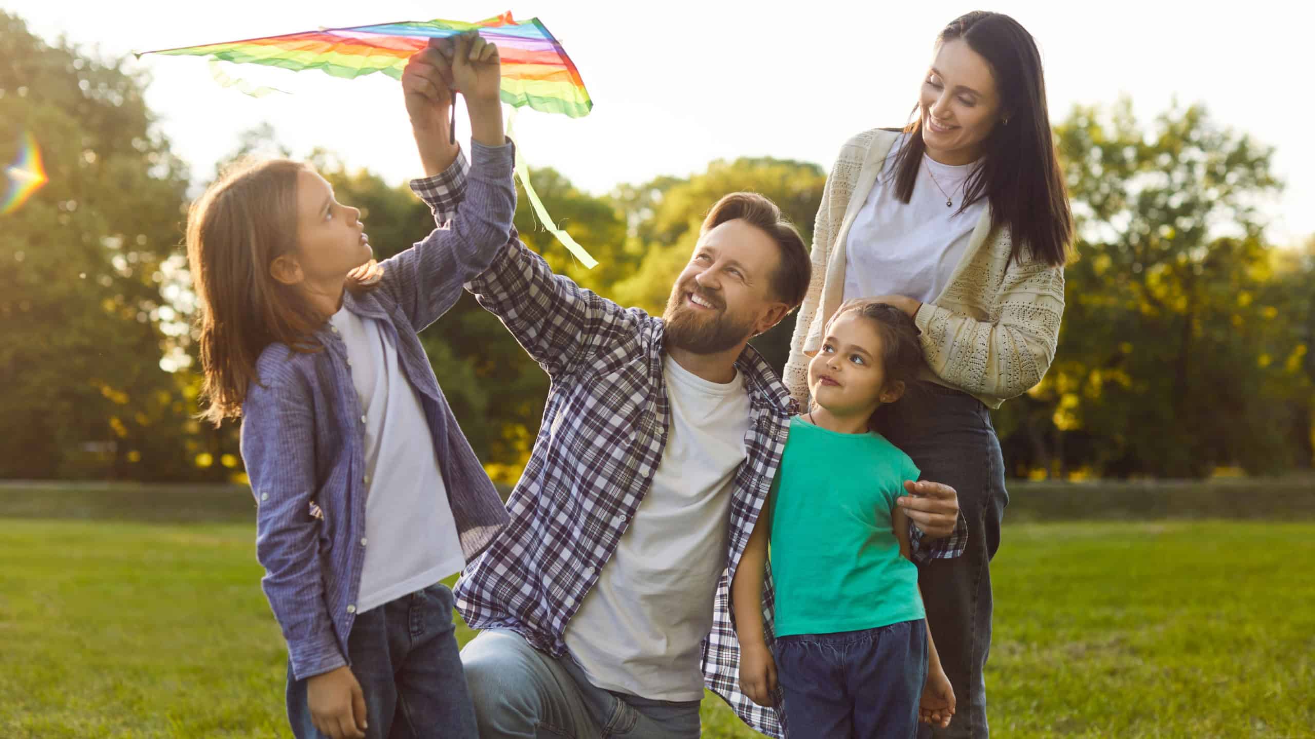 Happy young family spending quality time together outdoors and flying colorful kite in park. Smiling parents and children enjoying leisure activity and bonding during sunny weekend on fresh air.
