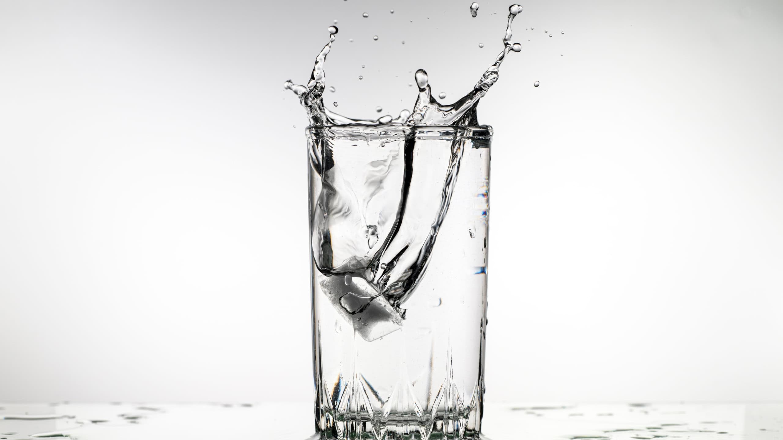 A glass of water with ice cubes in it is splashing water out of the glass. The water is cold and refreshing, and the ice cubes are melting, creating a splash. Concept of movement and energy