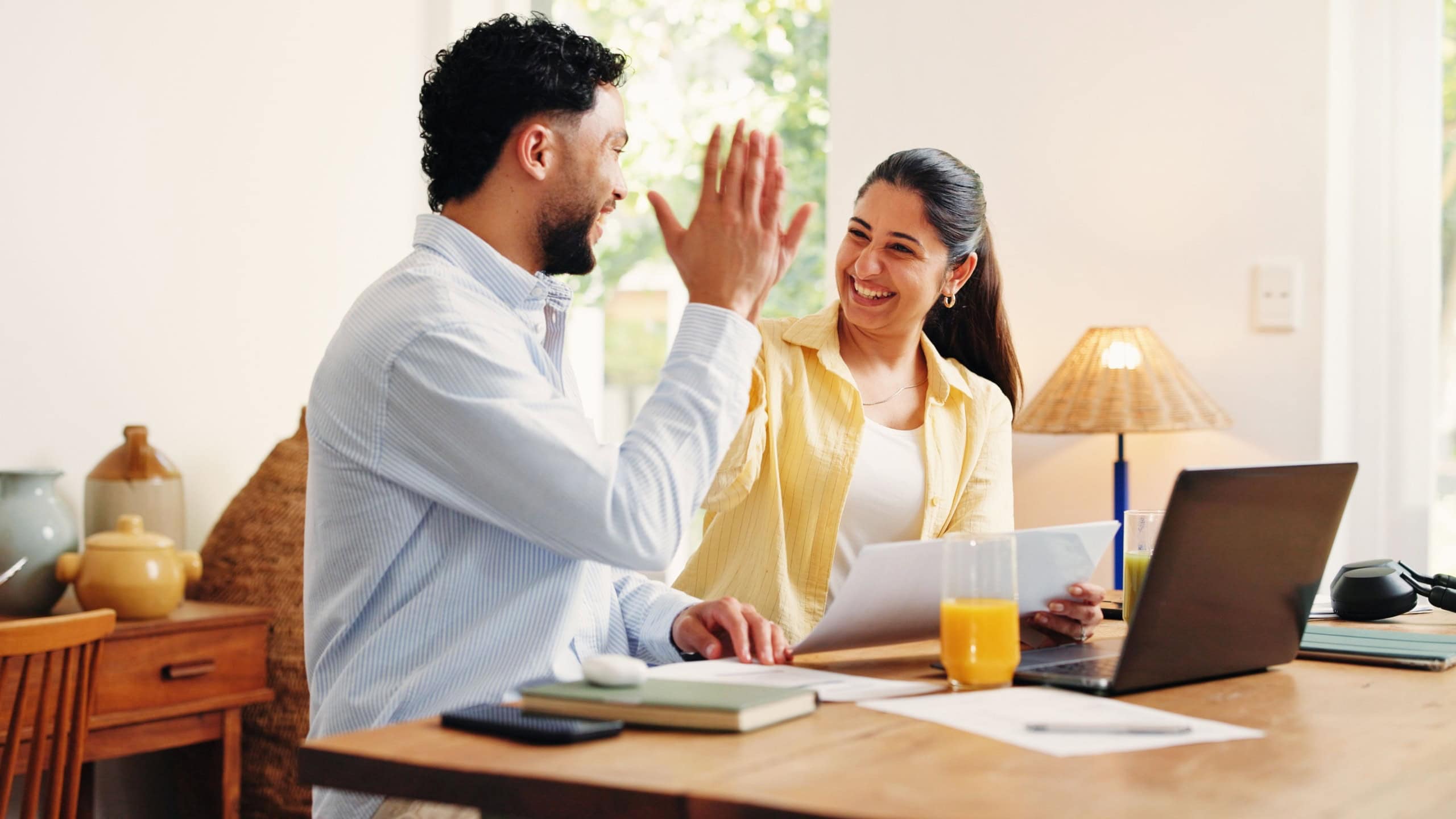 Documents, high five and couple in home with laptop for paying off bills, debt or mortgage. Happy, financial paperwork and man with woman for celebration on computer for internet banking for purchase