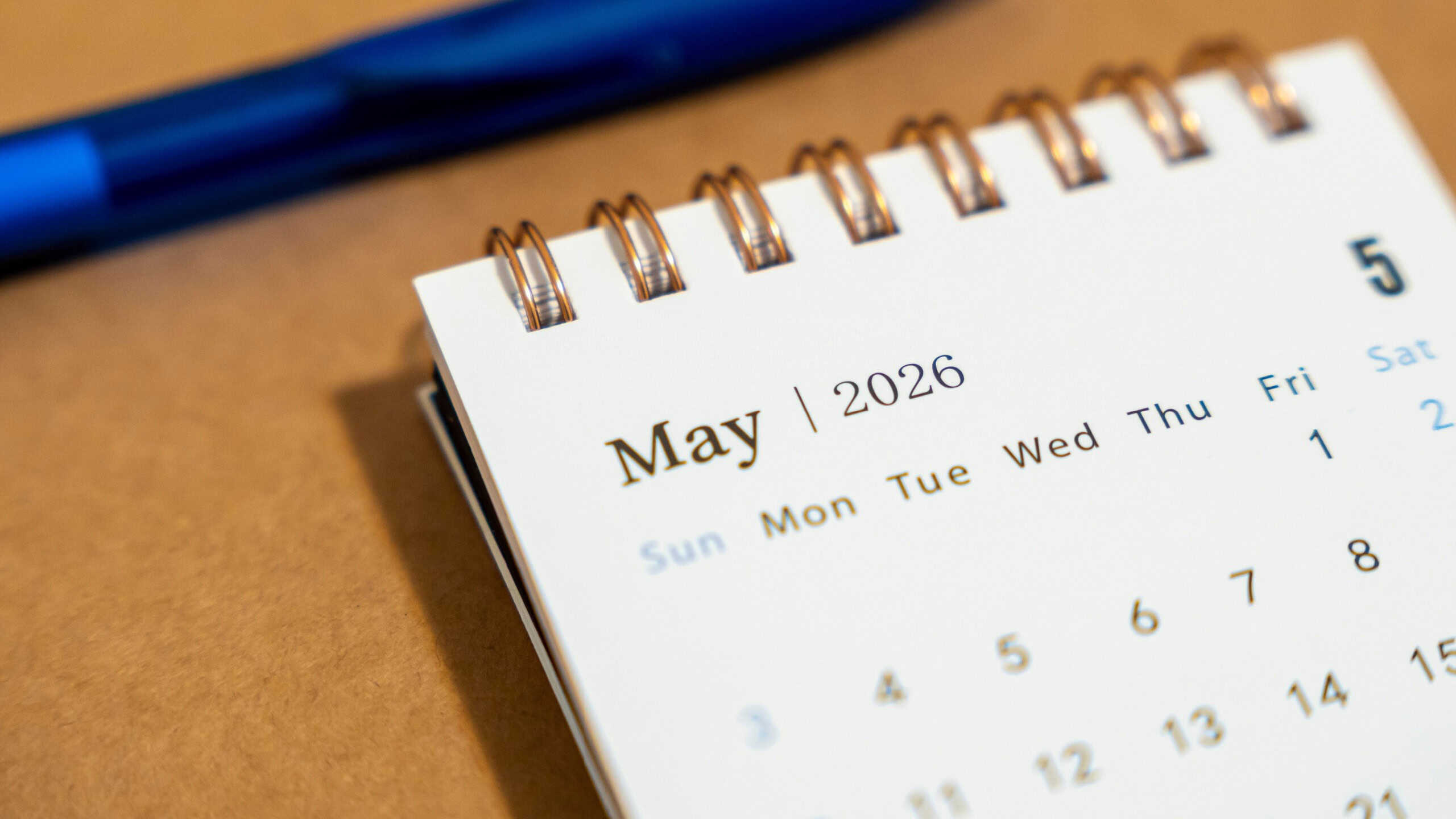 Calendar page displaying the month of May 2026, showcasing days of the week and dates. Jet black pen resting nearby on a light brown background, ideal for planning or scheduling.