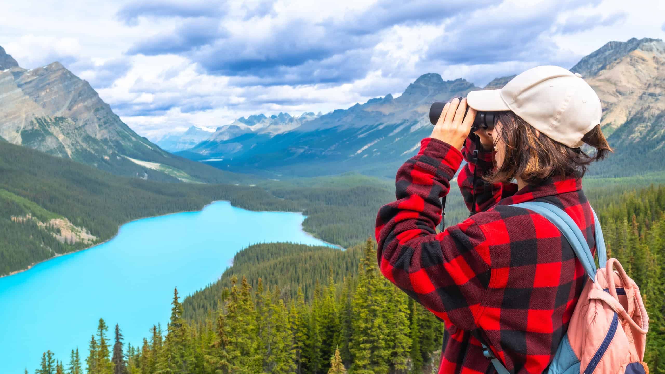 Female hiker using binoculars admires the stunning turquoise waters of peyto lake and majestic mountains in banff national park, alberta's breathtaking wilderness