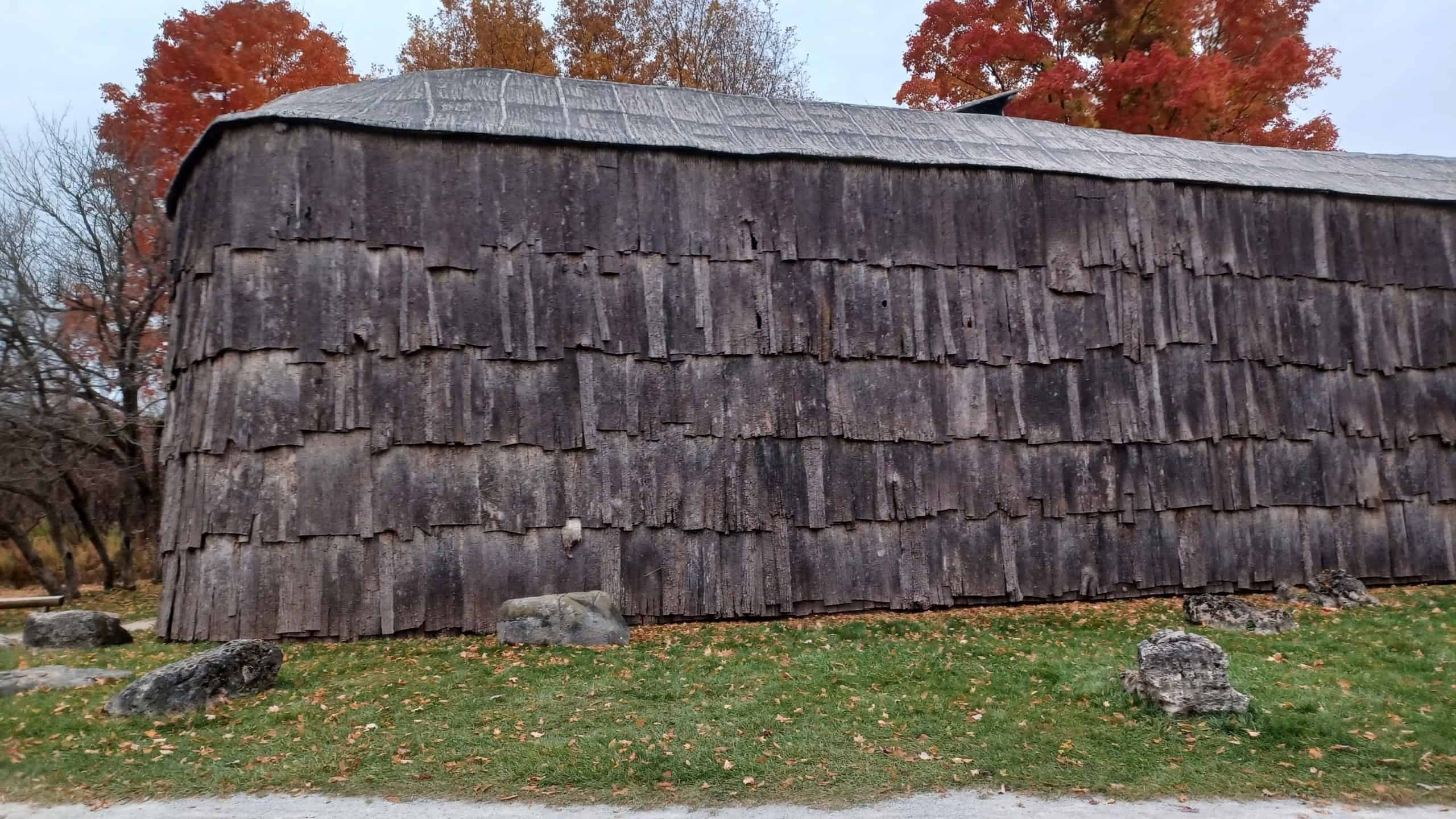 A large historical longhouse building made of bark sits under a cloudy sky.