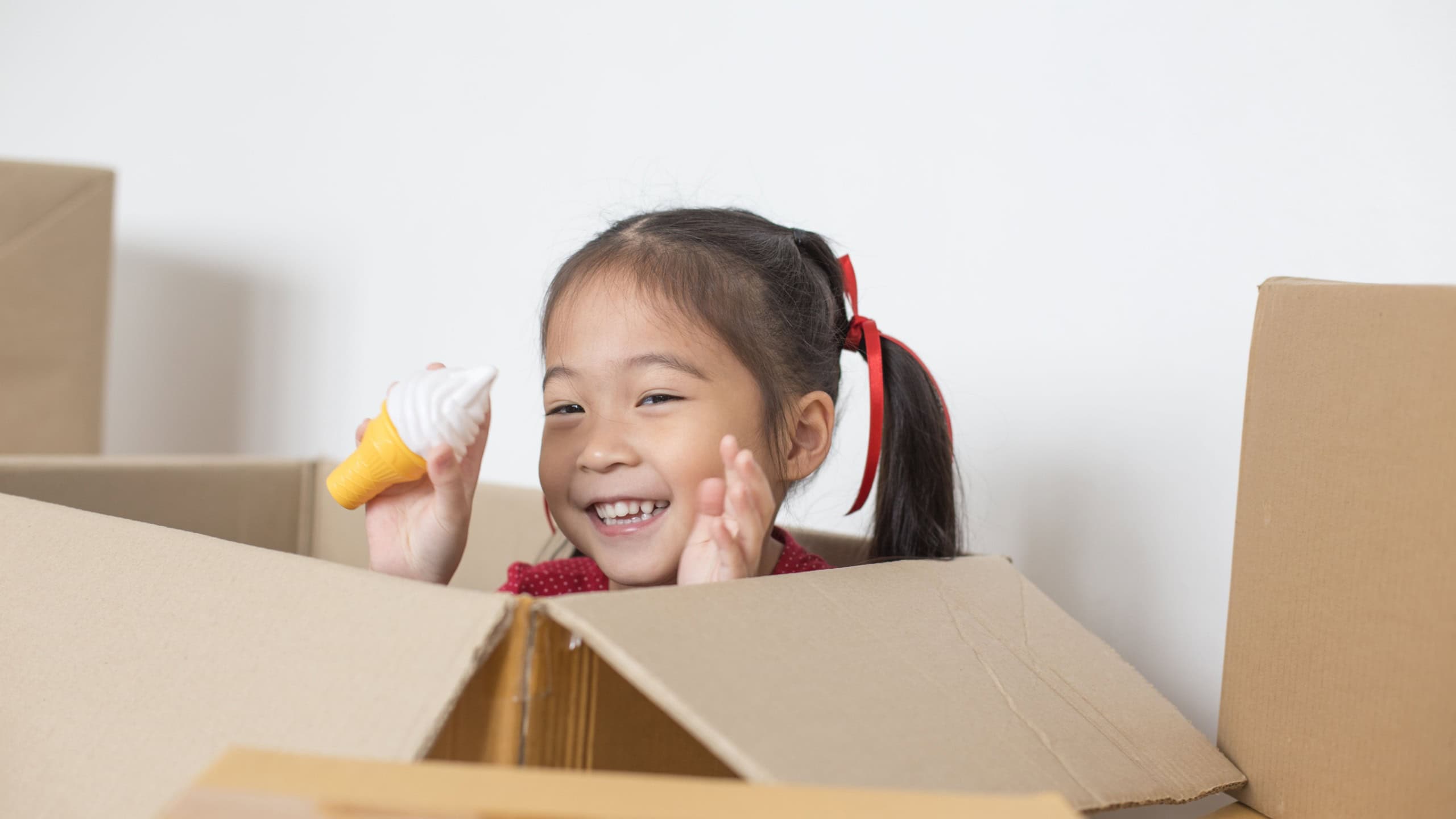 Asian Girl playing in the box at home. Kid sitting inside Box with Attractive smiling.